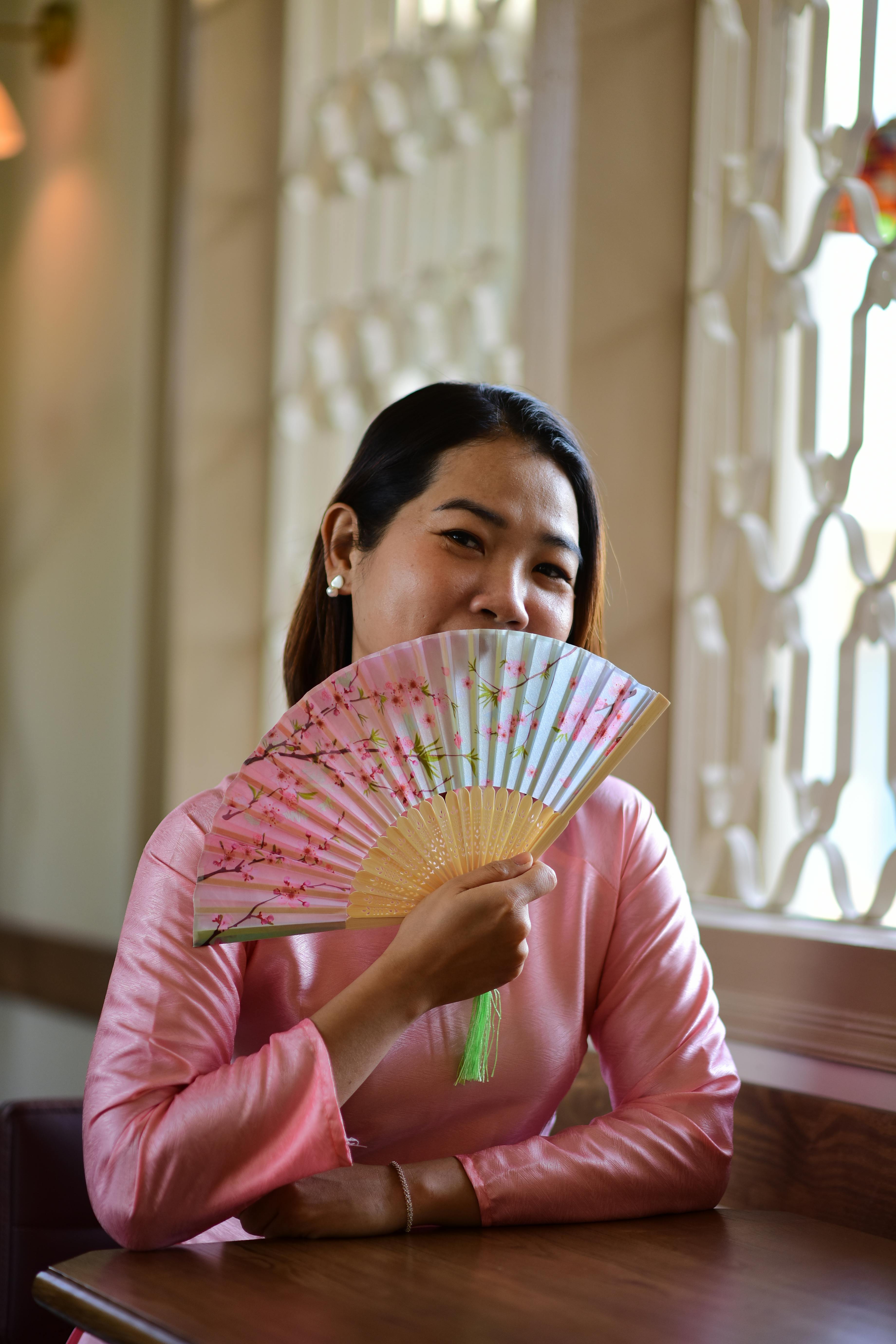 Gratis Smilende kvinne med blomstervifte i tradisjonell kjole innendørs. Arkivbilde