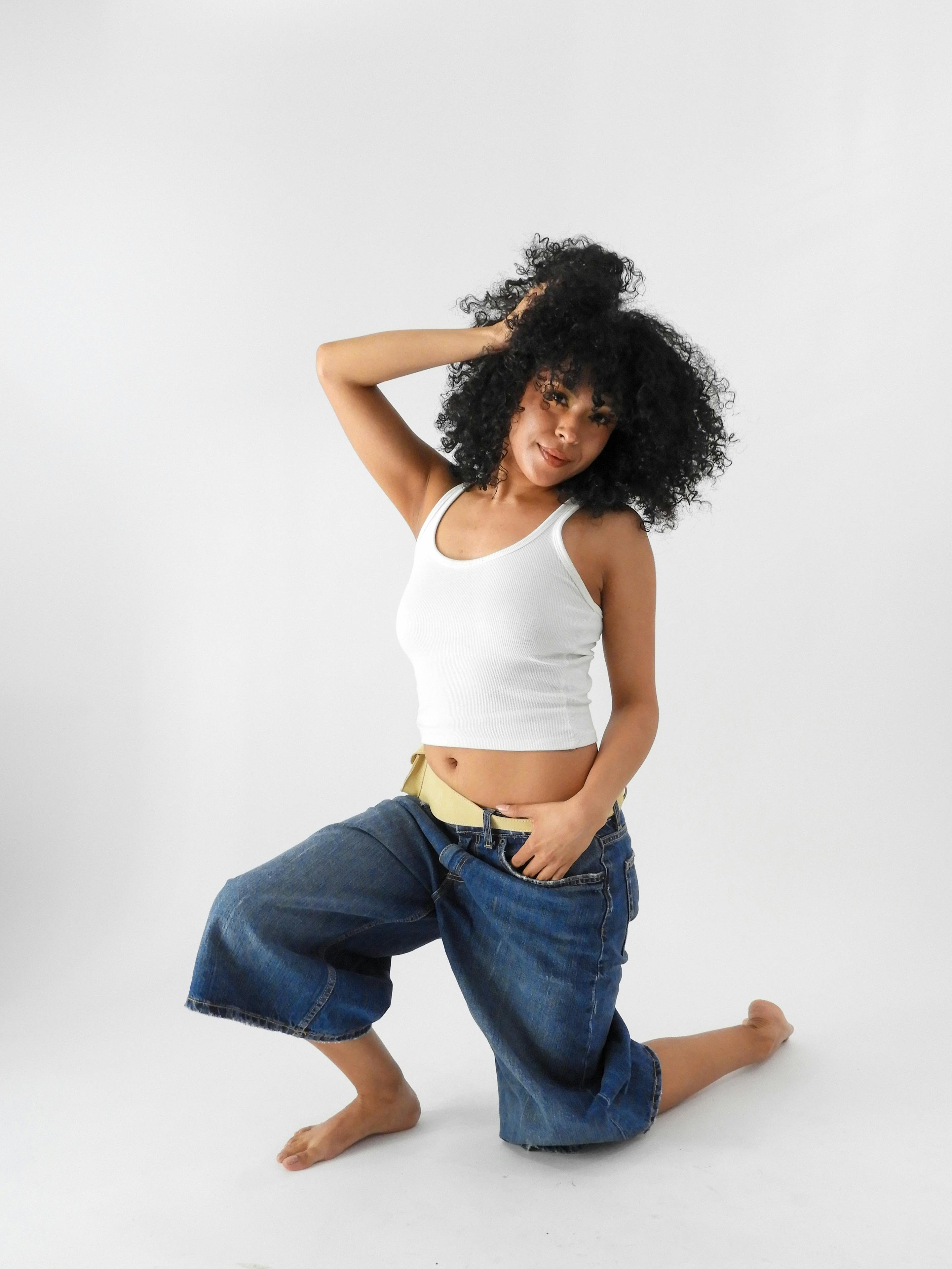 grátis Retrato artístico de uma mulher posando com confiança em um estúdio, vestindo roupas casuais e exalando força e estilo. Foto profissional