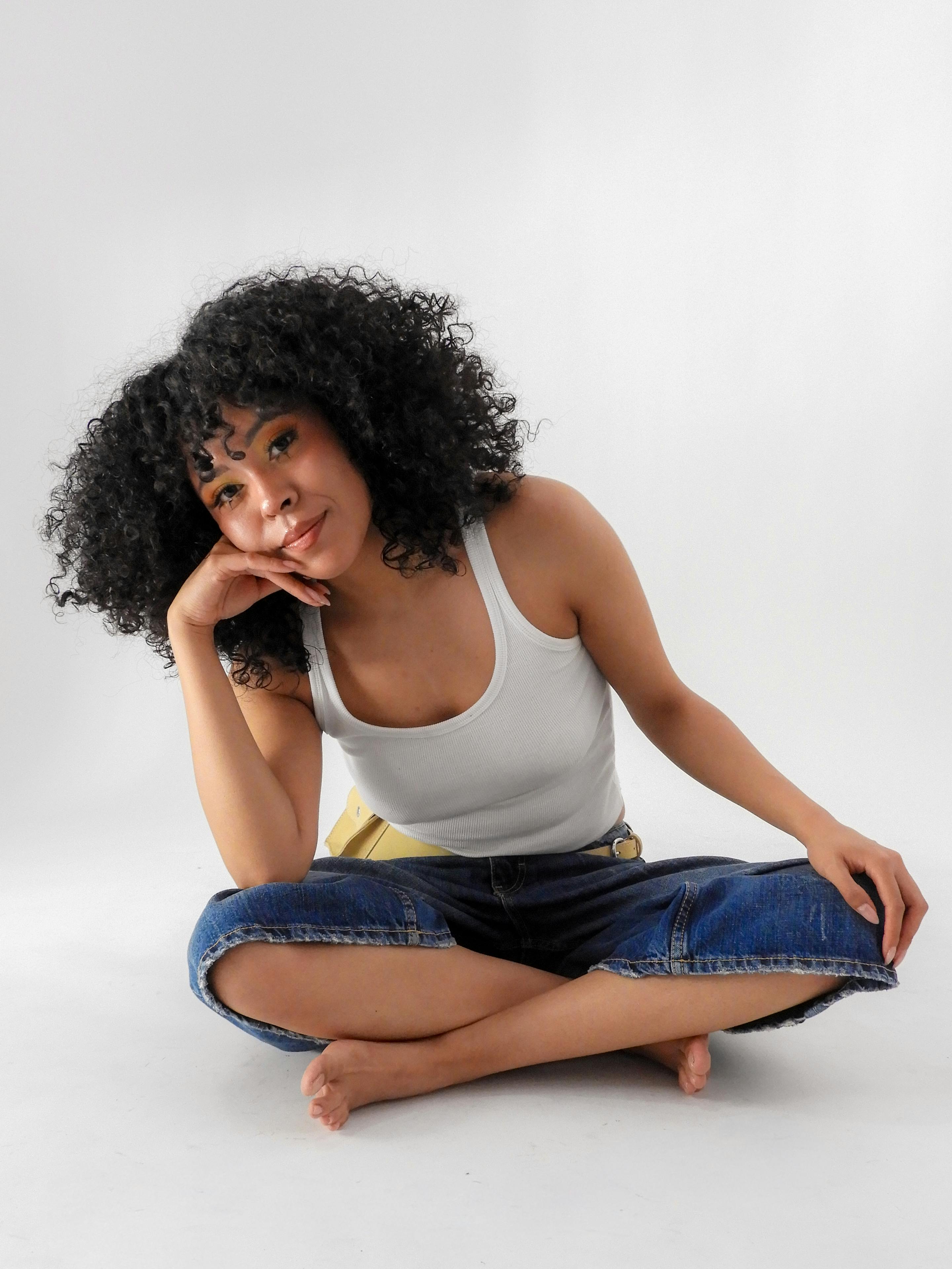 grátis Uma mulher de cabelos cacheados senta-se de pernas cruzadas, exalando confiança e simpatia. Foto profissional