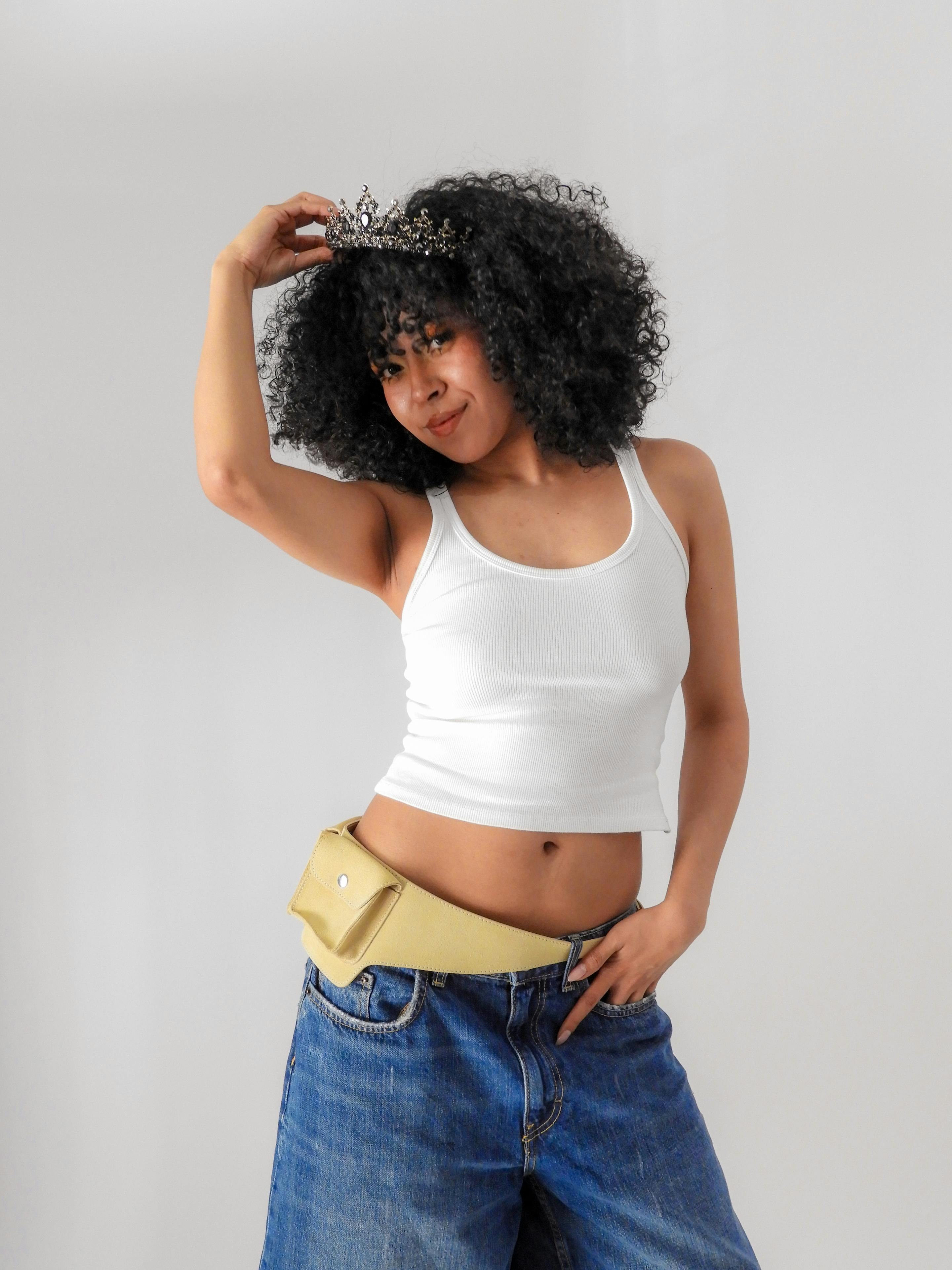 Gratuit O femeie elegantă, cu părul creț, pozează încrezătoare, purtând o tiară și o ținută casual. Perfectă pentru concepte de modă și stil de viață. Fotografie de stoc