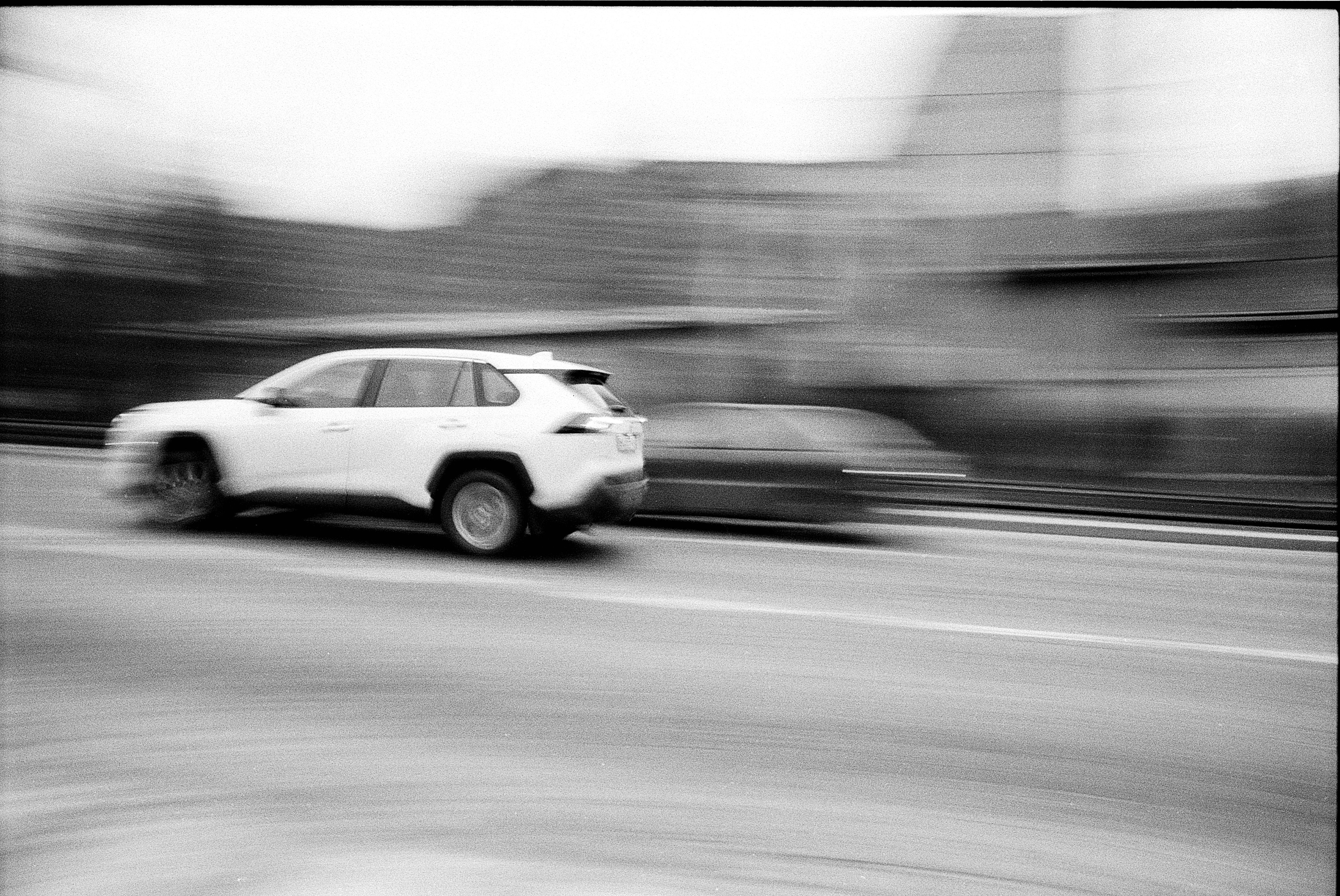 Black and white image capturing cars in motion blur on a city road.