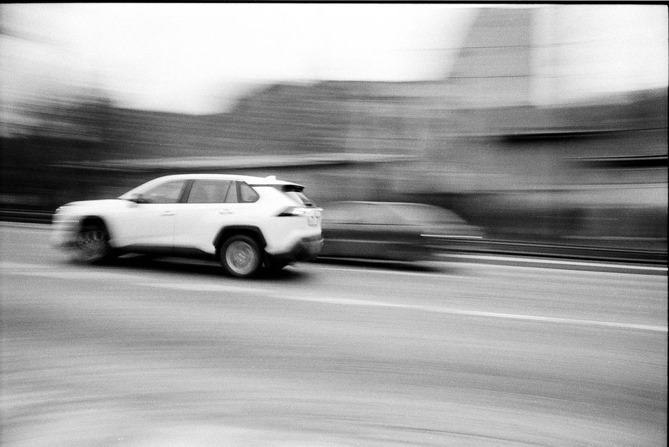 Black and white image capturing cars in motion blur on a city road.