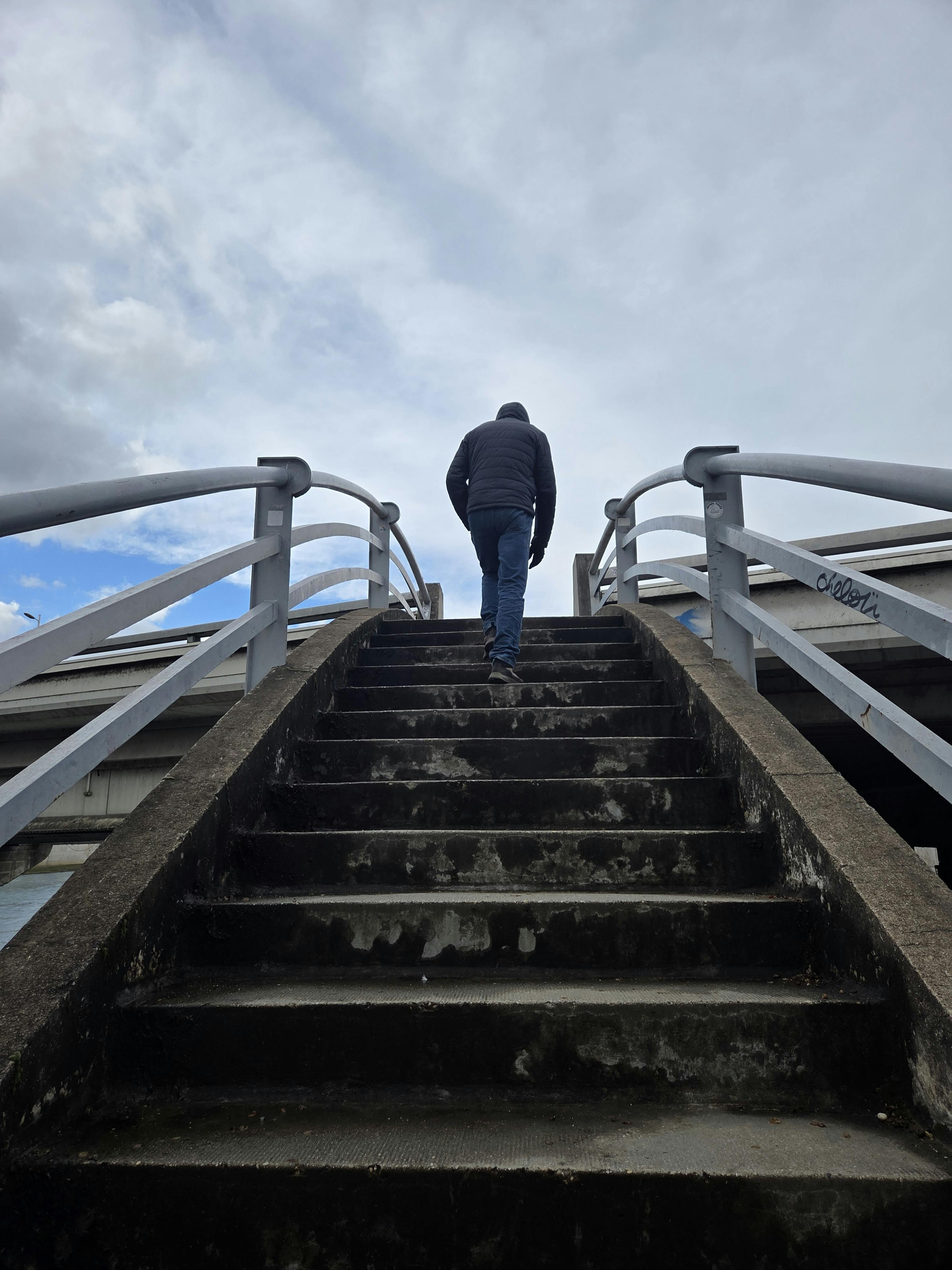 무료 구름이 낀 극적인 배경을 뒤로하고 한 사람이 다리 위 계단을 오르고 있다. 스톡 사진