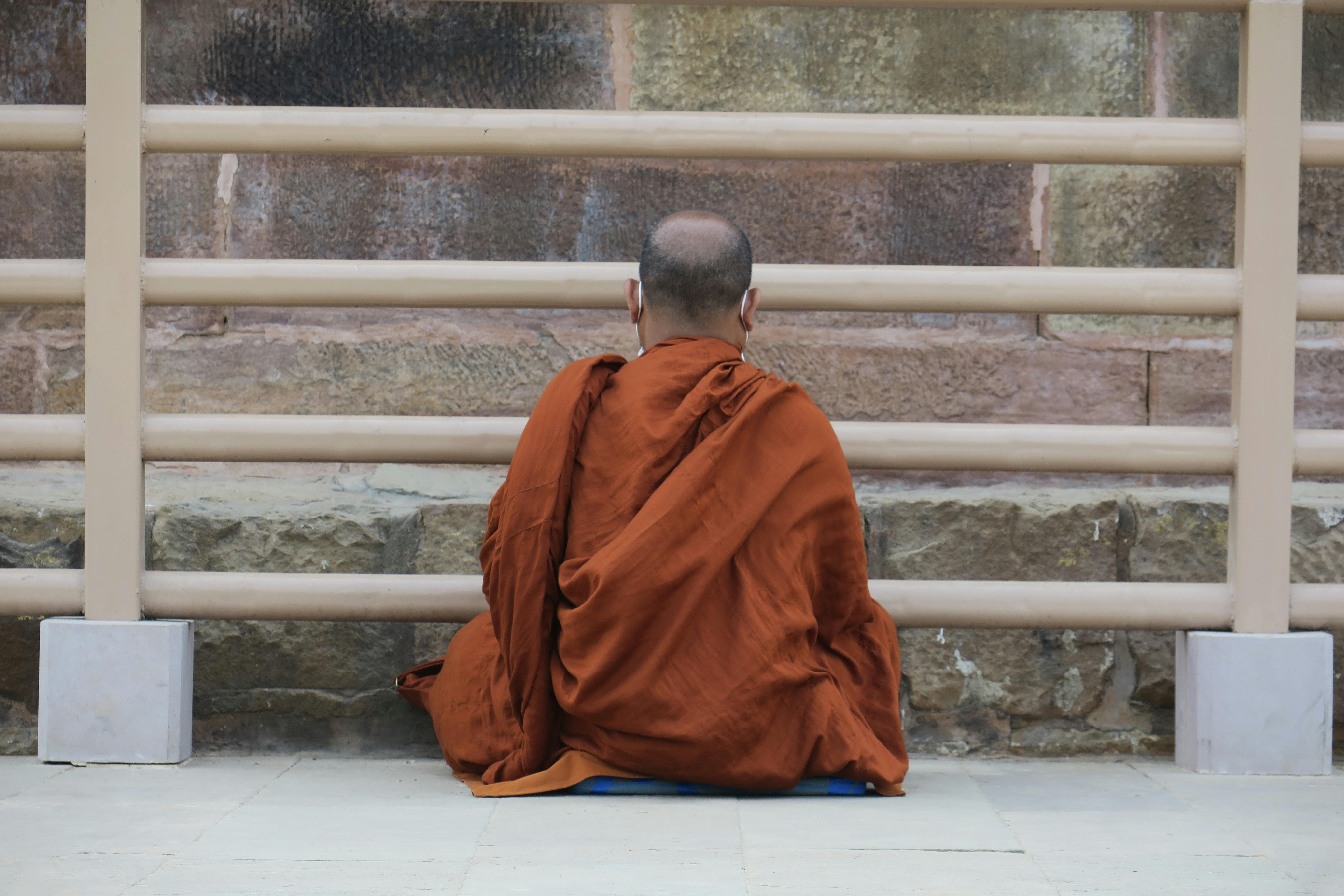 gratis Een monnik in oranje gewaden mediteert vredig tegen een stenen muur en straalt rust en introspectie uit. Stockfoto