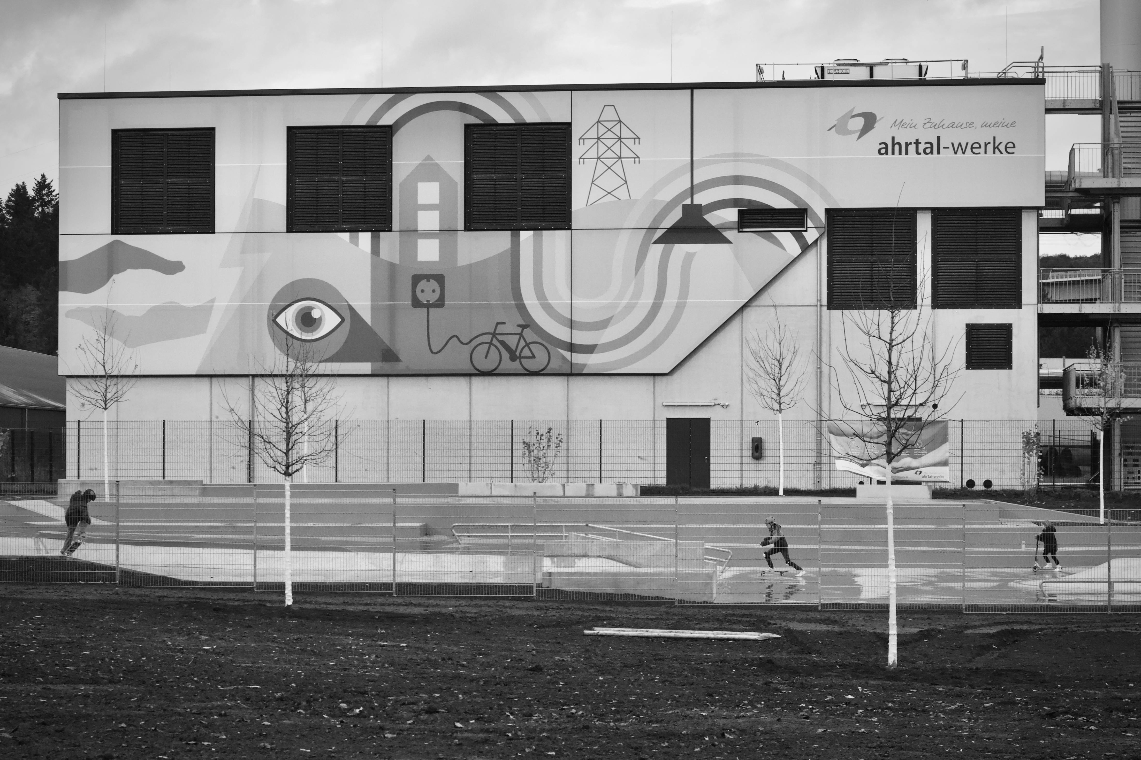 Free Black and white photo of industrial building with mural, people running in foreground. Stock Photo
