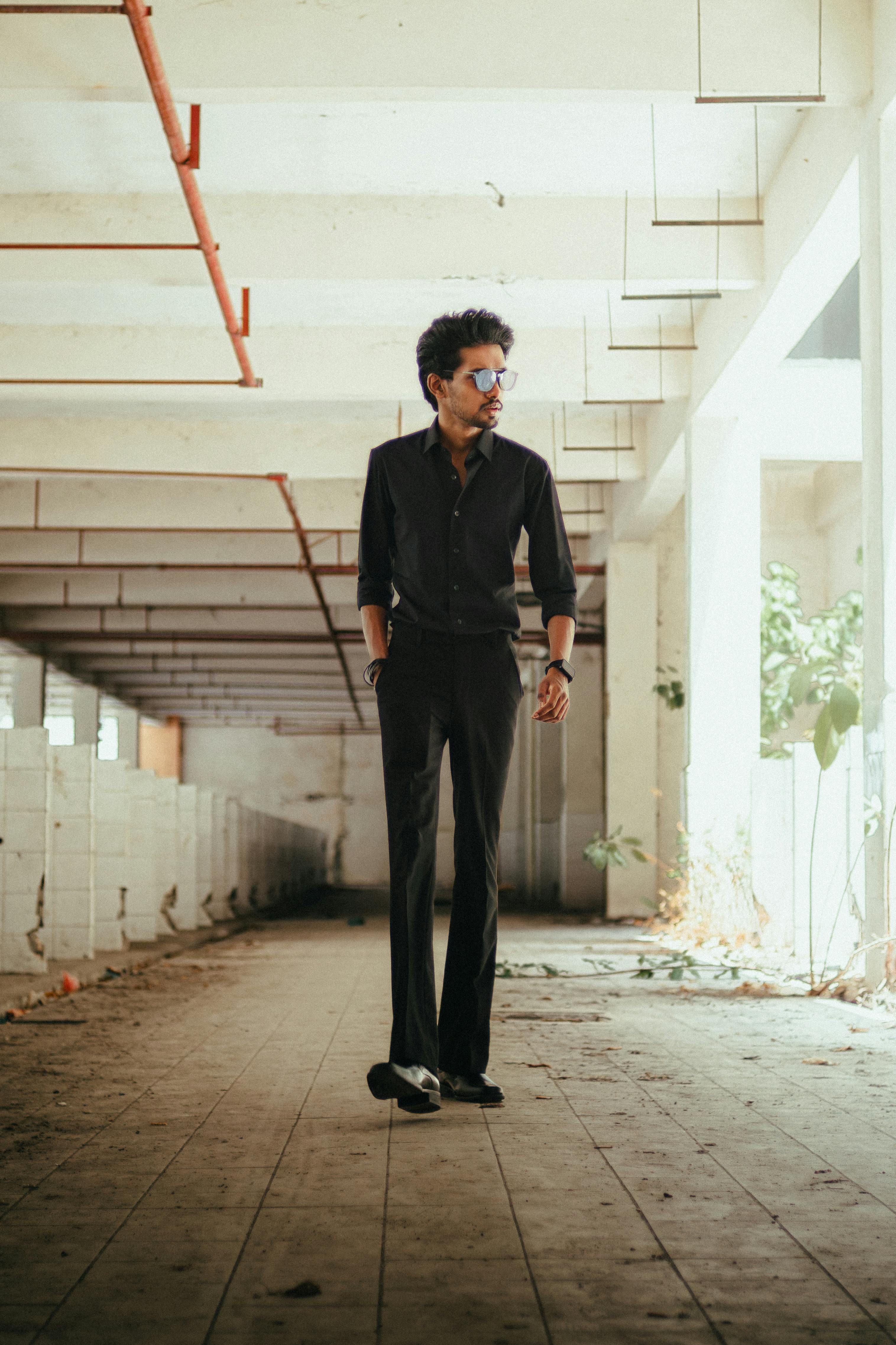 免費 一名身穿黑色服裝的男子自信地走過廢棄的工業區，散發出一種時尚而神秘的氣息。 圖庫相片