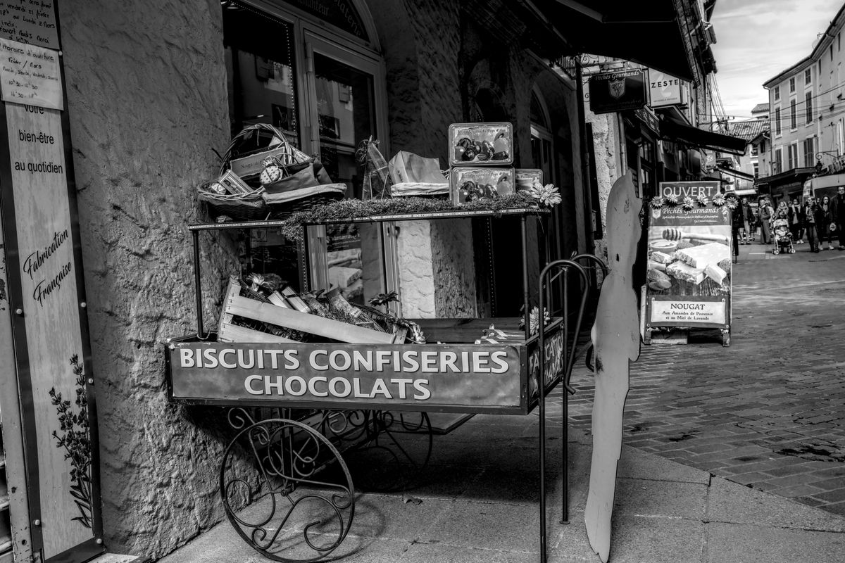 Black and white photo of a French candy and chocolate cart on a cobblestone street.