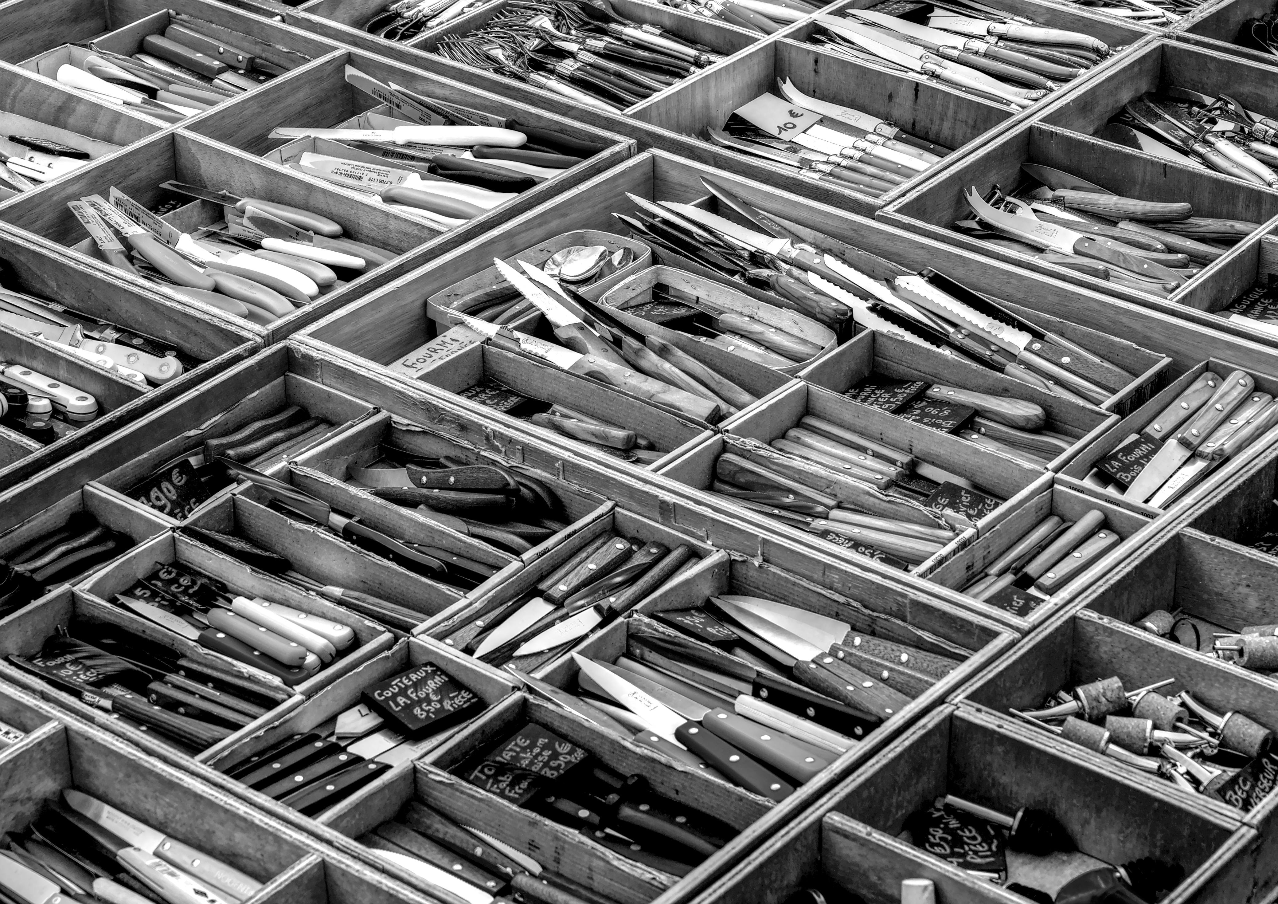 ingyenes Egy részletes fekete-fehér fénykép késekről, amelyeket faládákban állítottak ki egy szabadtéri piacon. Stockfotó