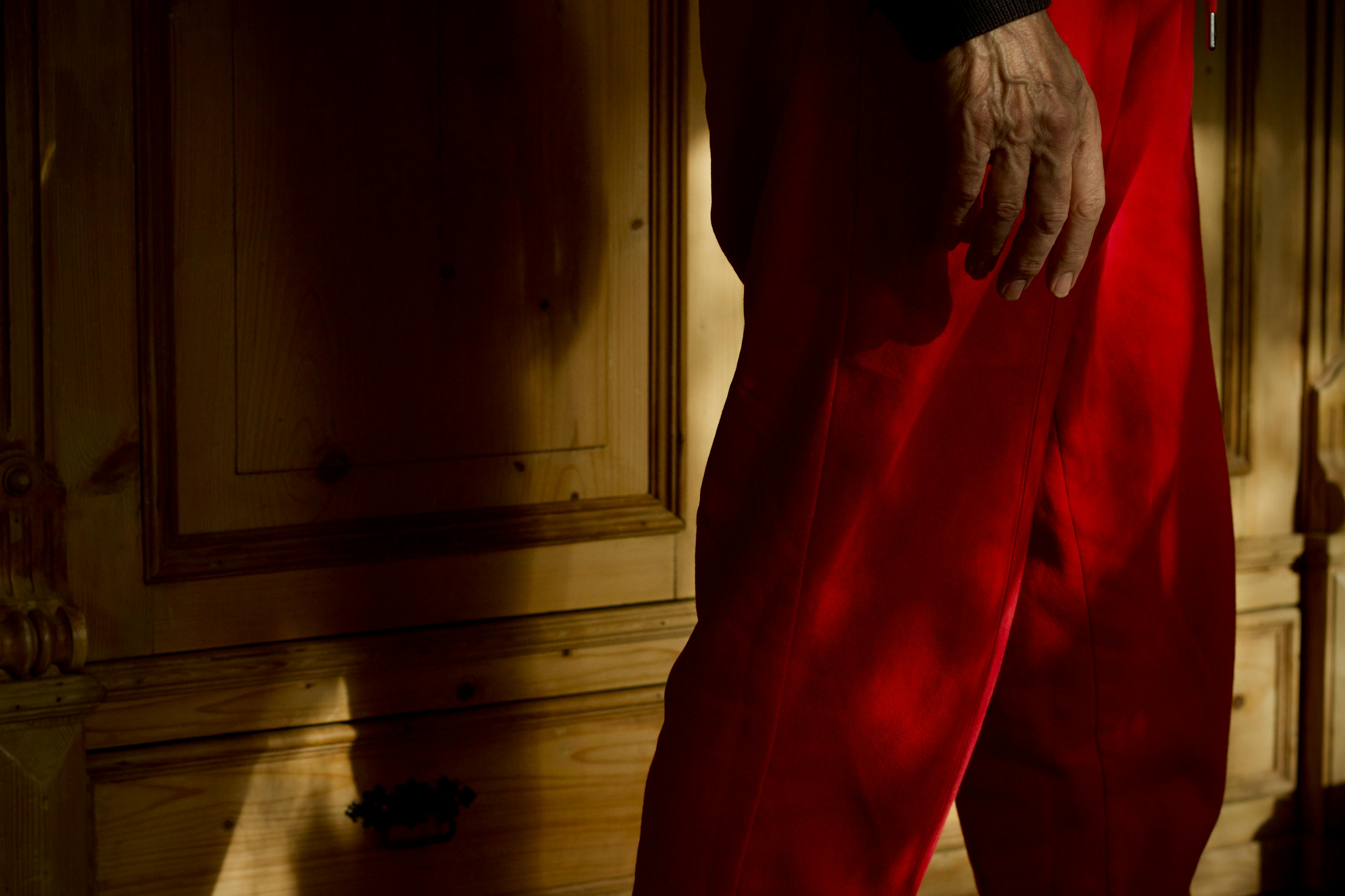 bezplatná Detailní pohled na mužskou ruku a červené kalhoty s dřevěným nábytkem na pozadí uvnitř. Základová fotografie