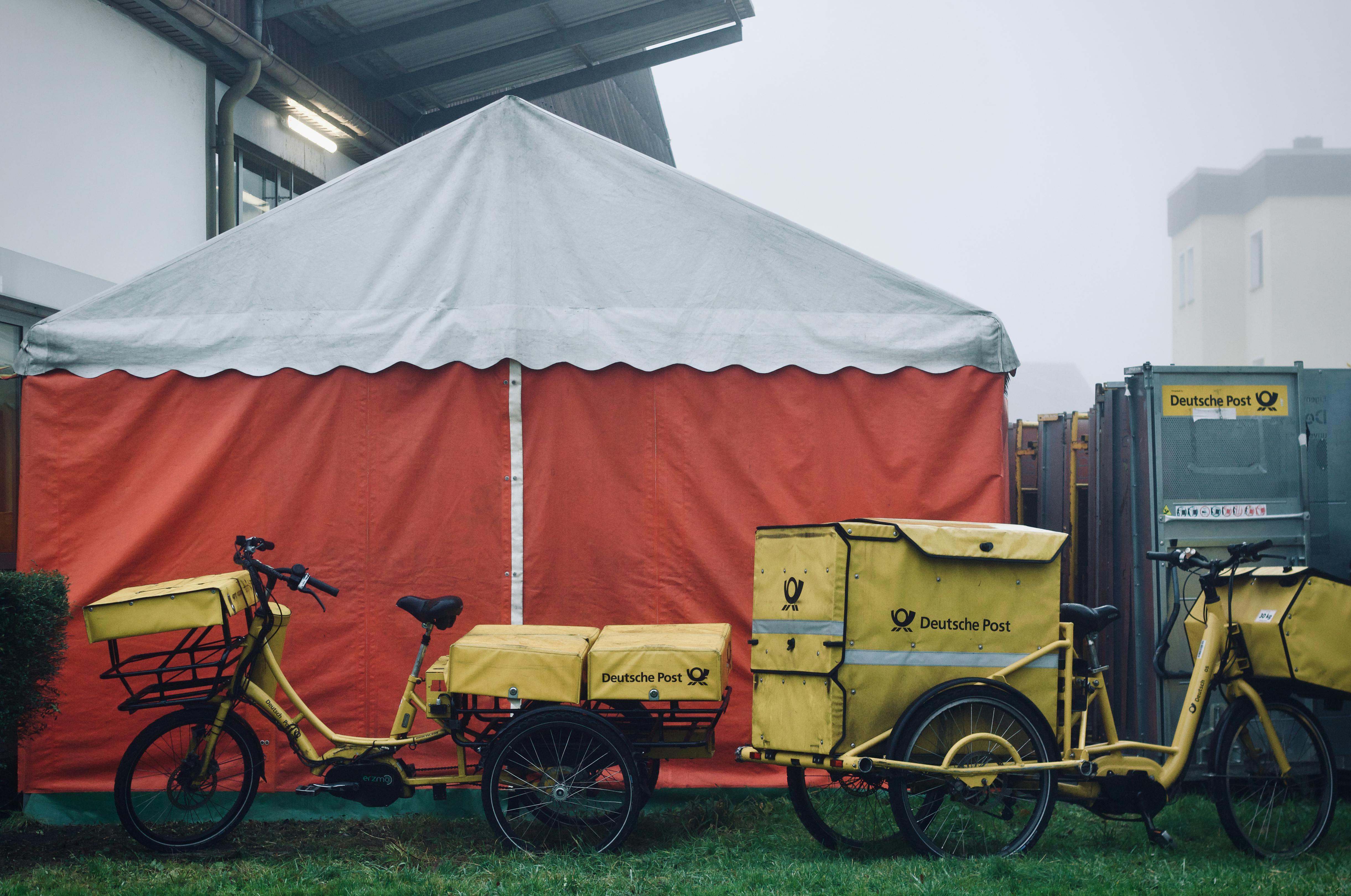 免费 在雾气弥漫的环境中，三辆黄色的德国邮政送货自行车停放在一个橙色的帐篷旁。 素材图片