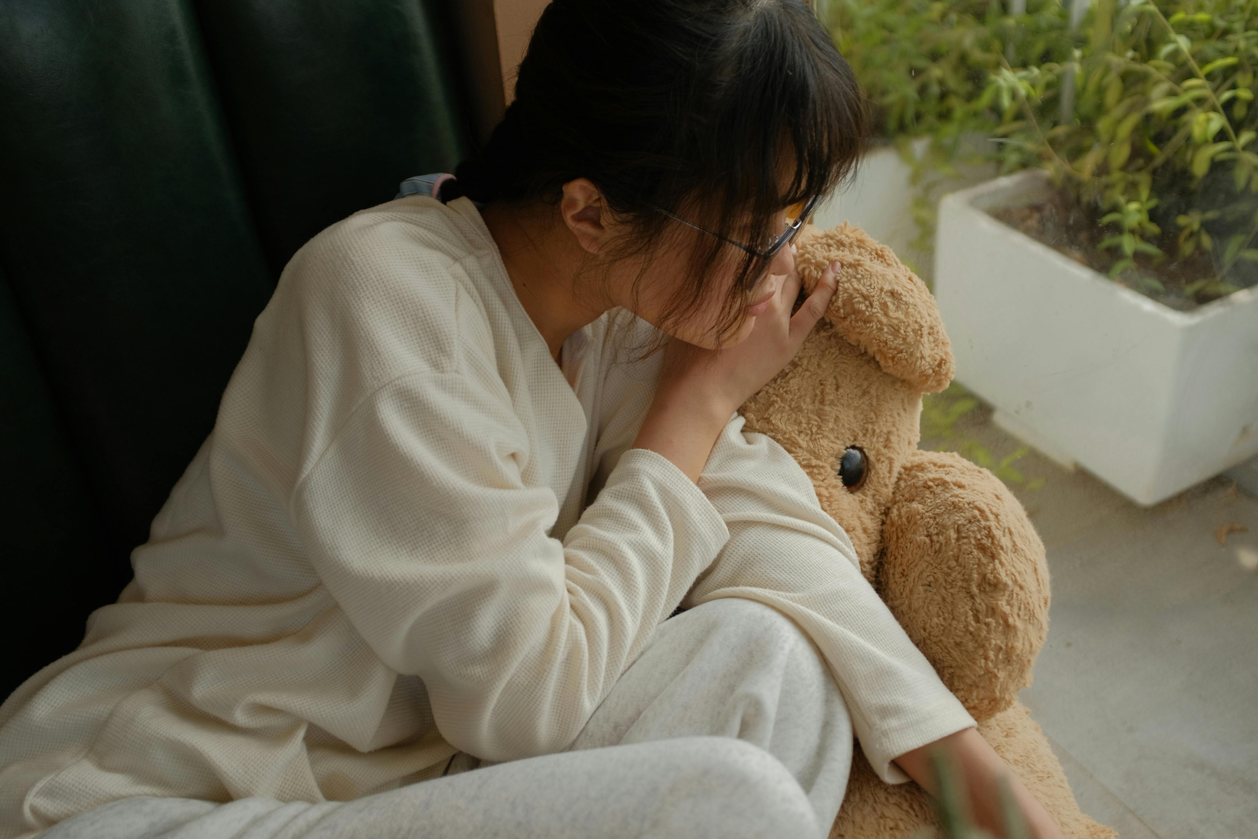 Miễn phí Một cô gái trẻ trong trang phục thường ngày đang thư giãn bên cửa sổ cùng một chú gấu bông. Ảnh lưu trữ