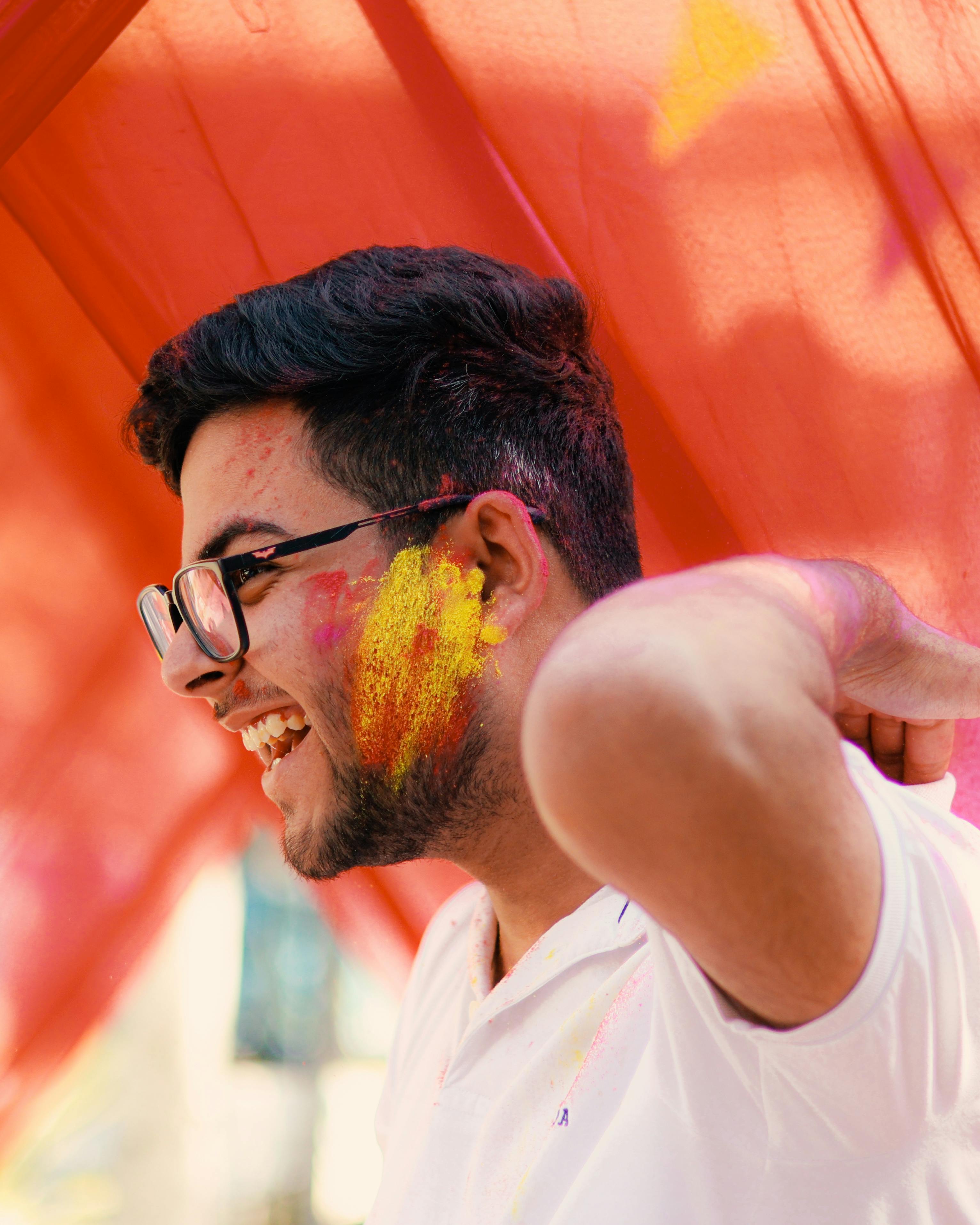 ฟรี ชายหนุ่มยิ้มแย้มแจ่มใสขณะสนุกสนานกับสีสันสดใสของเทศกาลโฮลีในบรรยากาศกลางแจ้ง คลังภาพถ่าย