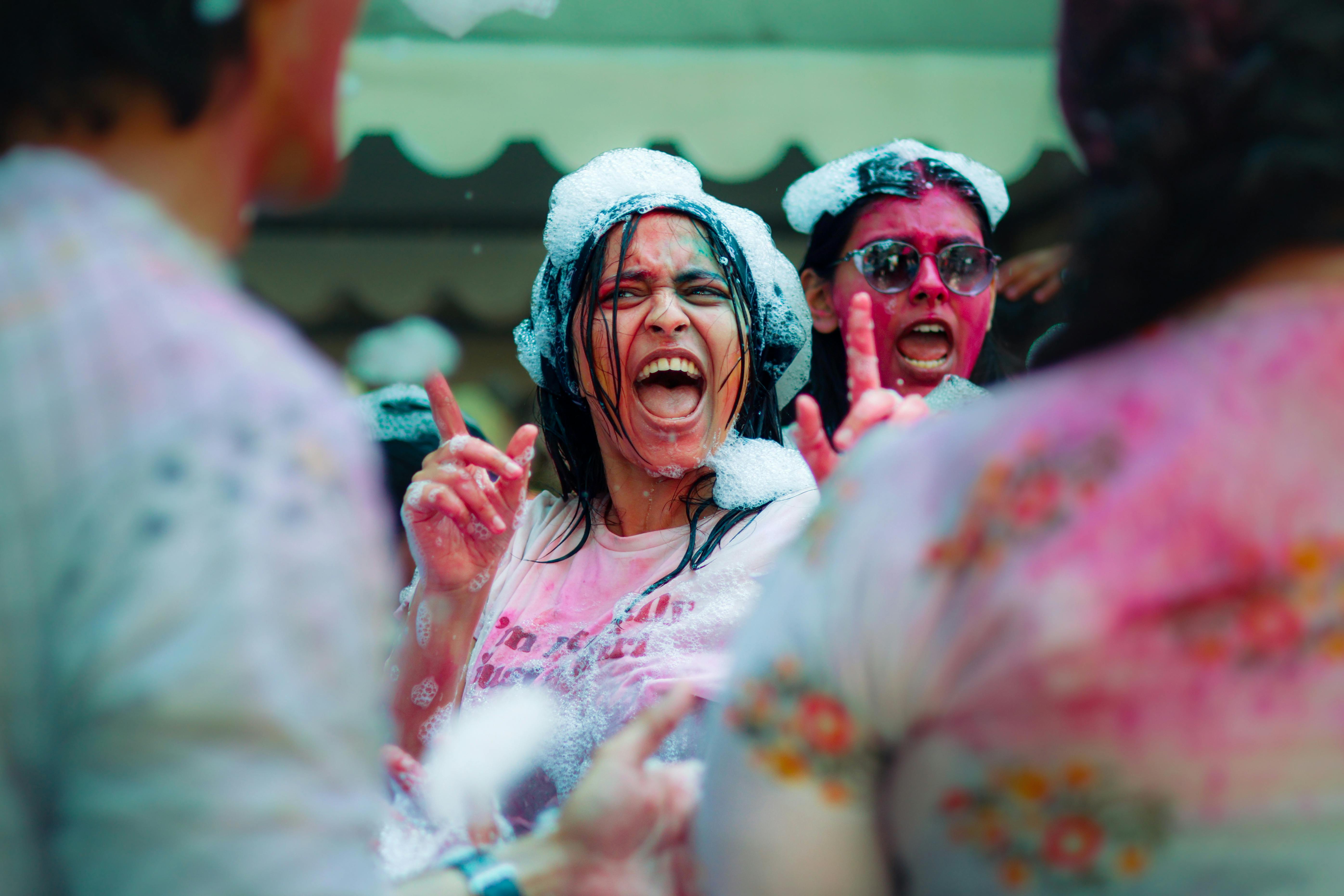 People celebrating in a powder-splashed crowd, laughing and cheering with colorful paint on their faces and clothes