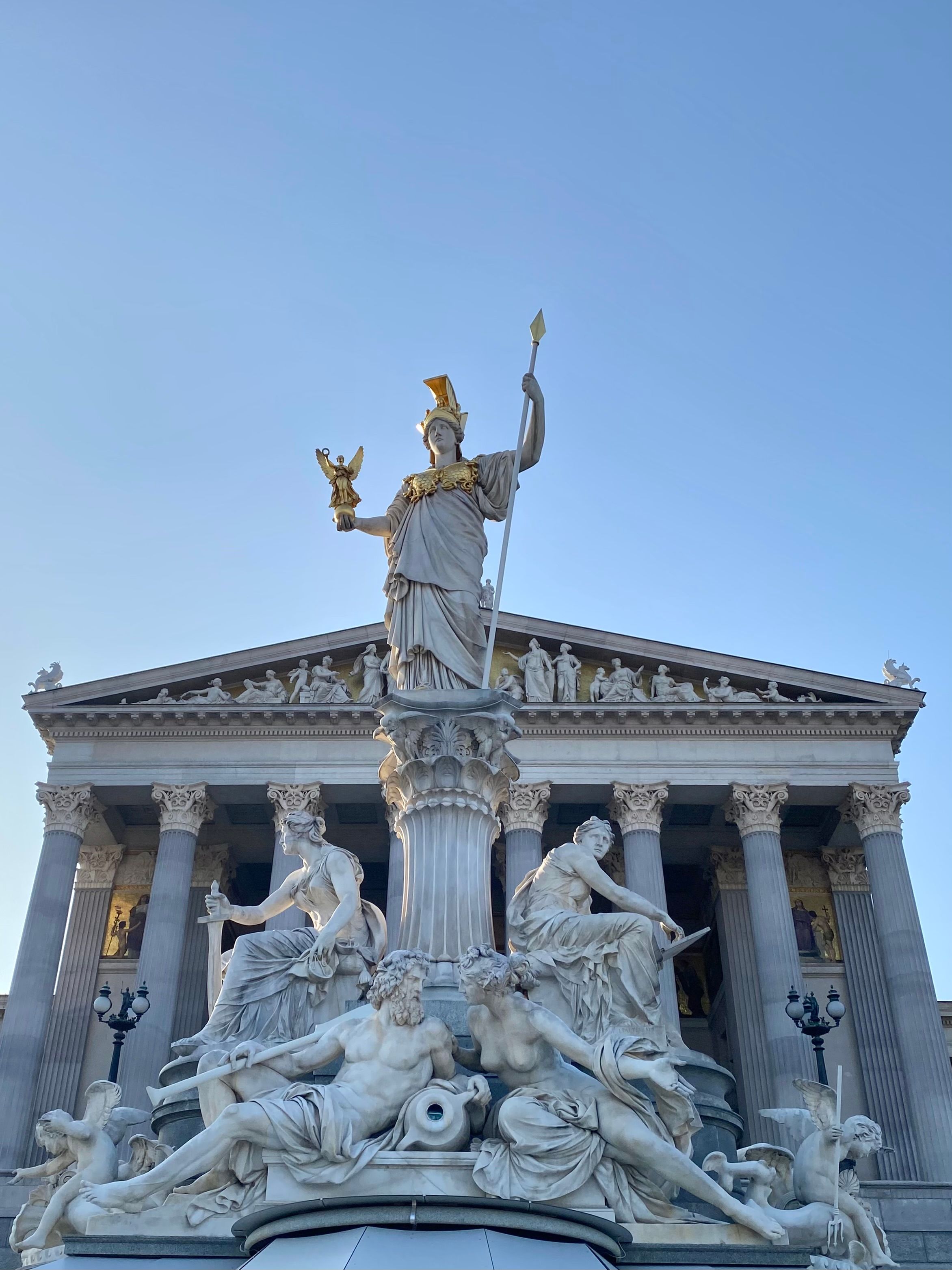 The Pallas Athena Fountain in front of Vienna's Austrian Parliament Building, bathed in daylight.