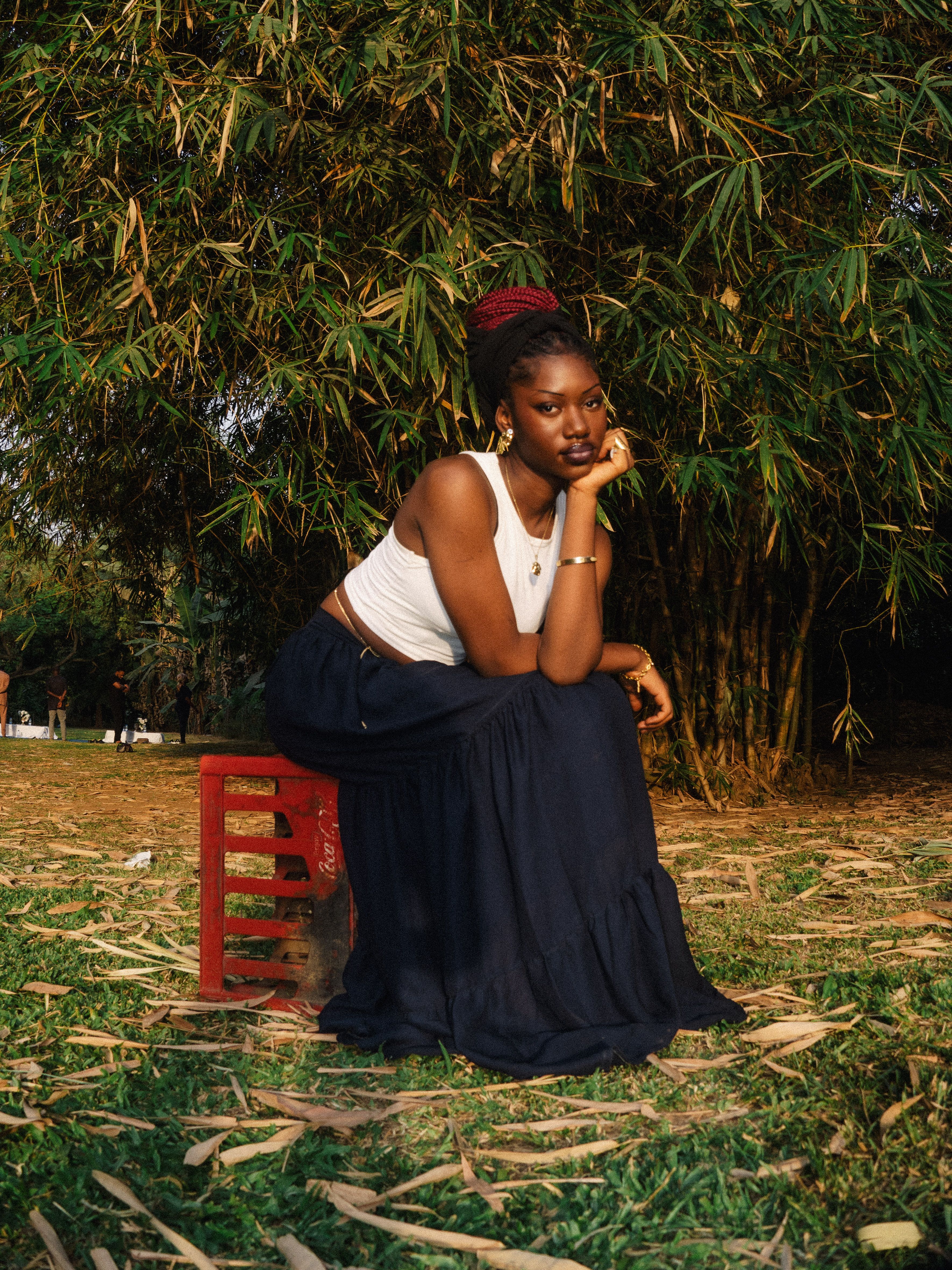 Portrait of a young woman sitting on a stool outdoors in Abuja, Nigeria, surrounded by lush greenery.