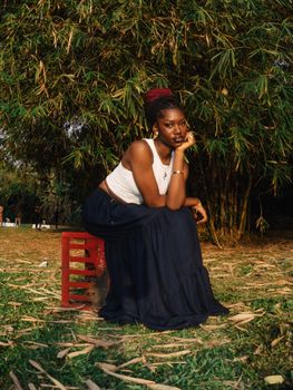 Portrait of a young woman sitting on a stool outdoors in Abuja, Nigeria, surrounded by lush greenery.