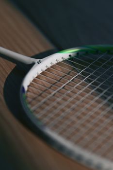 Detailed view of a badminton racket lying on a wooden floor with focused strings, perfect for sports-related themes.