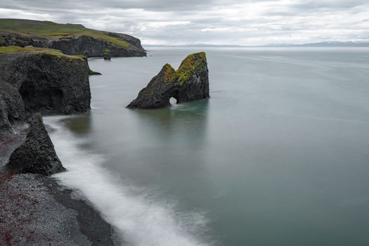 Long exposure of basalt cliffs with mossy rock formations and calm ocean waves.