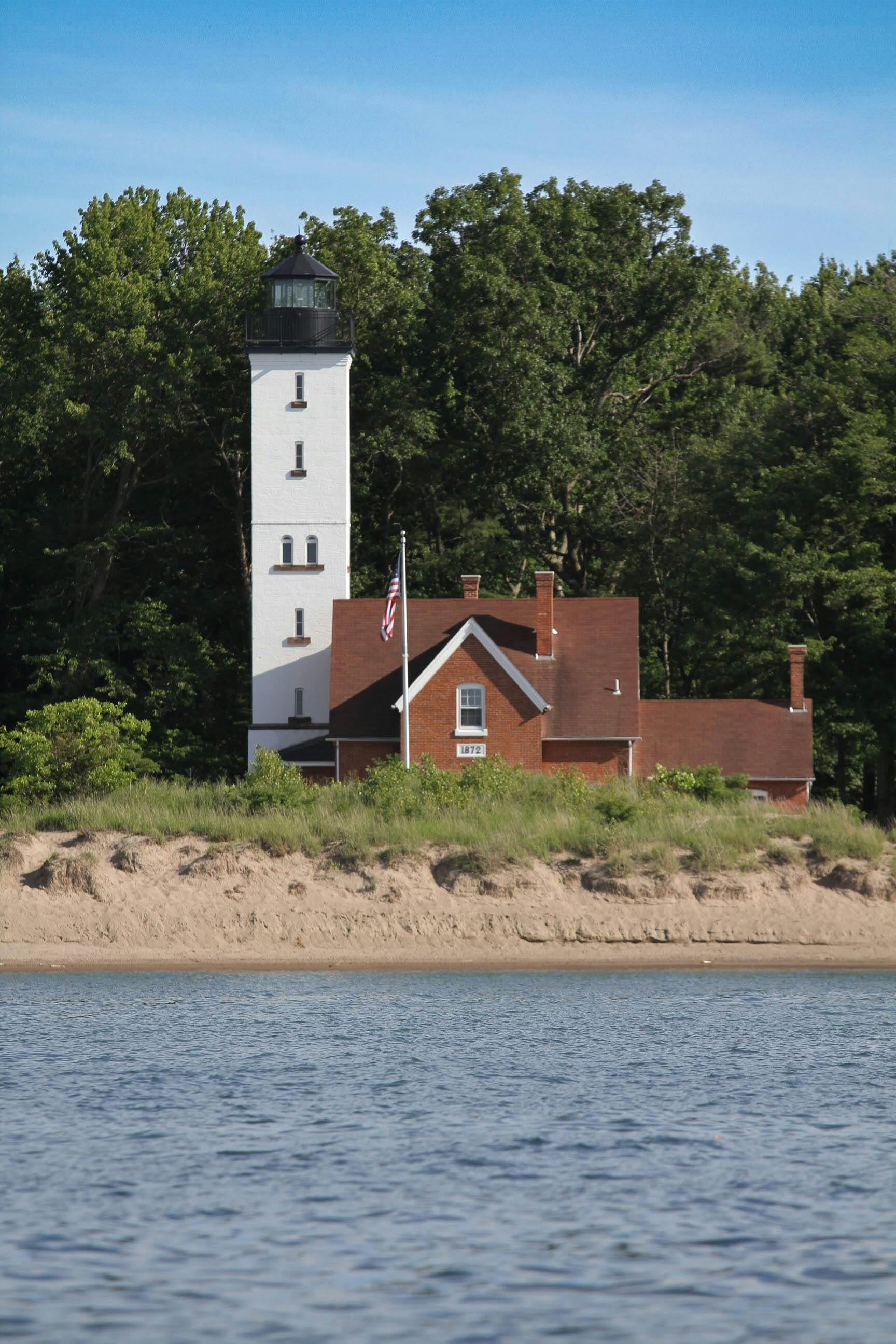Gratis Un faro classico si erge maestoso lungo le rive sabbiose del lago Michigan, circondato da una vegetazione lussureggiante. Foto a disposizione