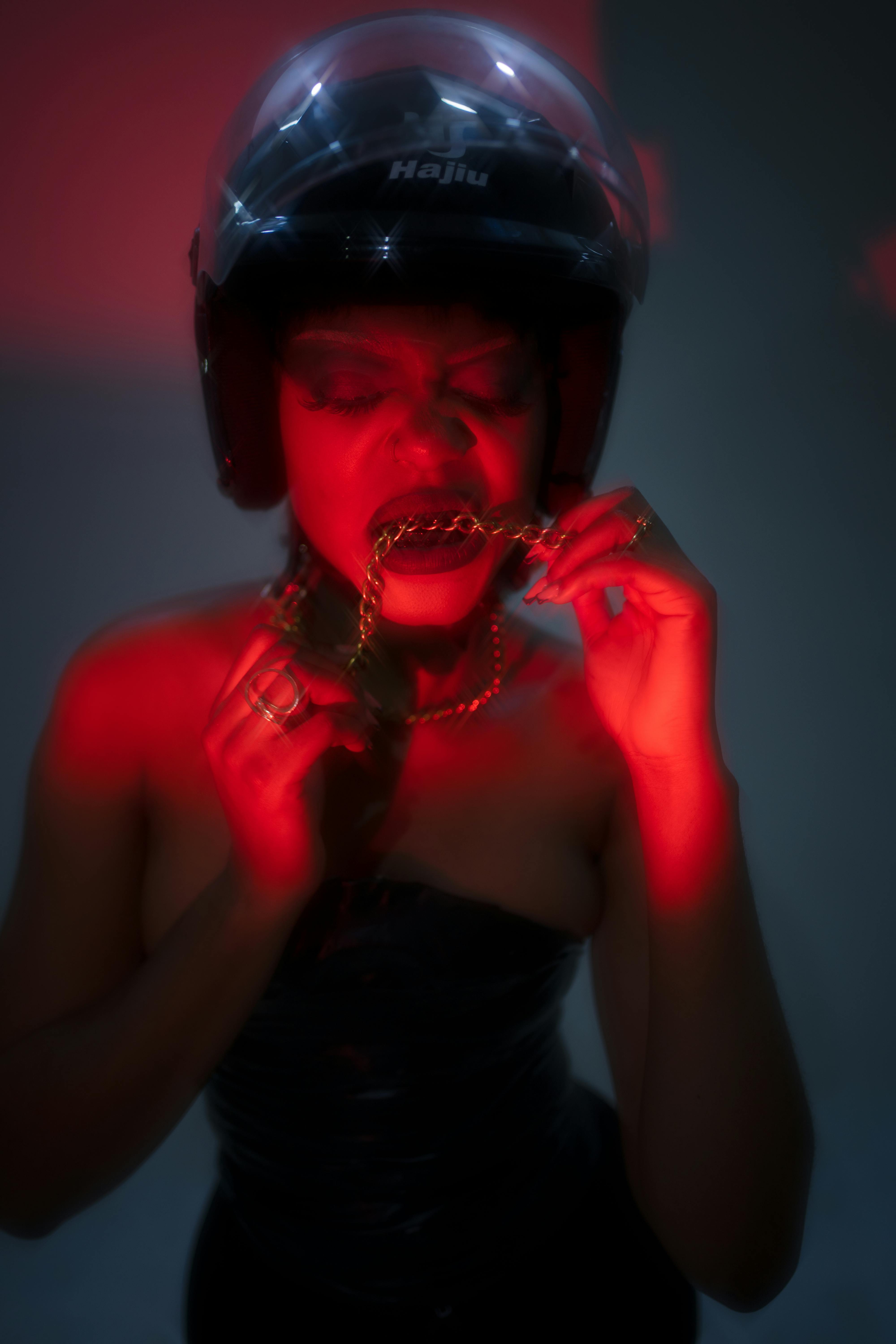Gratis Retrato artístico de una mujer con casco, bañada en luz roja, mordiendo una cadena. Foto de stock