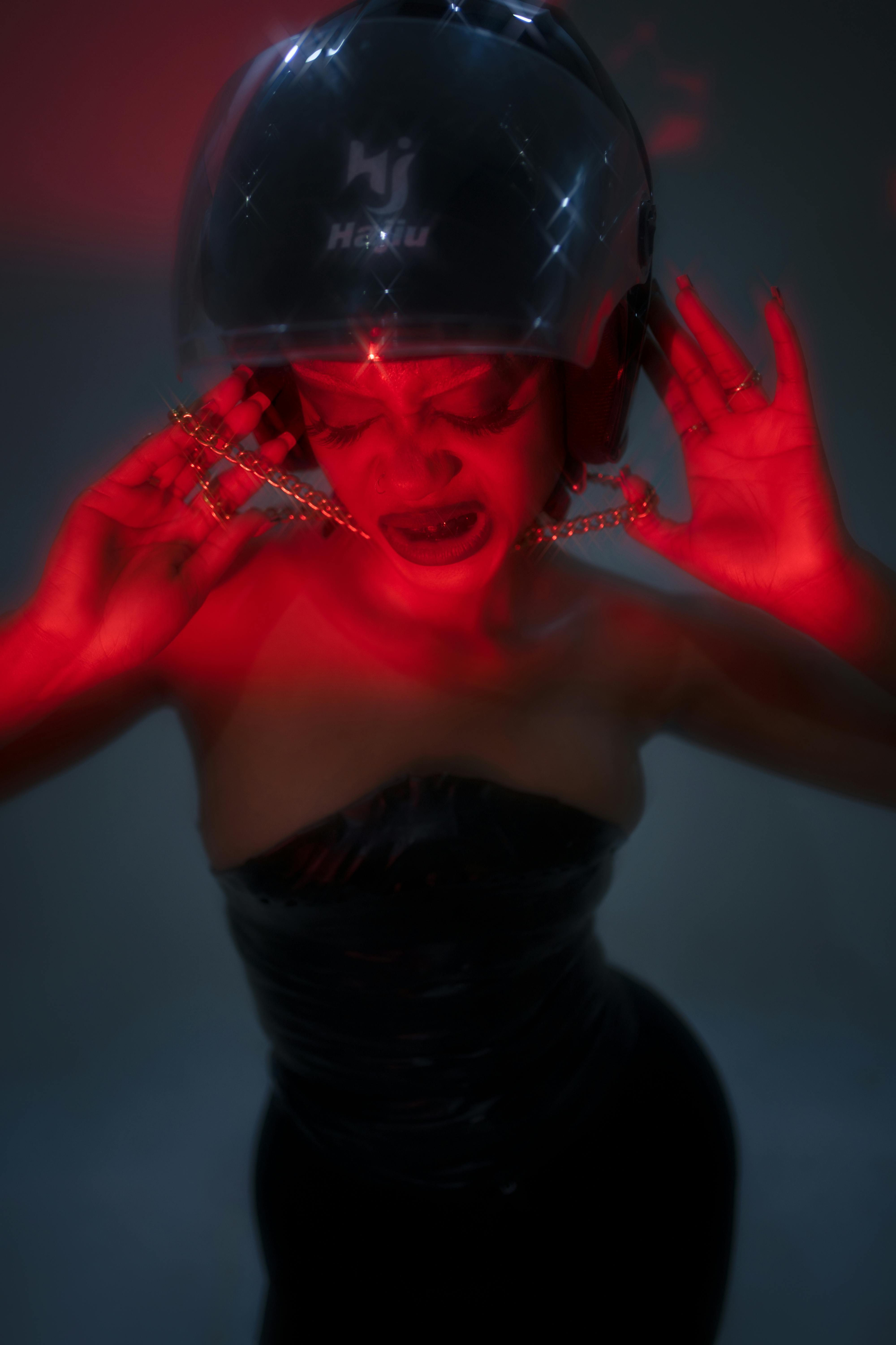 grátis Uma mulher usando capacete e joias, iluminada por uma dramática luz vermelha. Foto profissional
