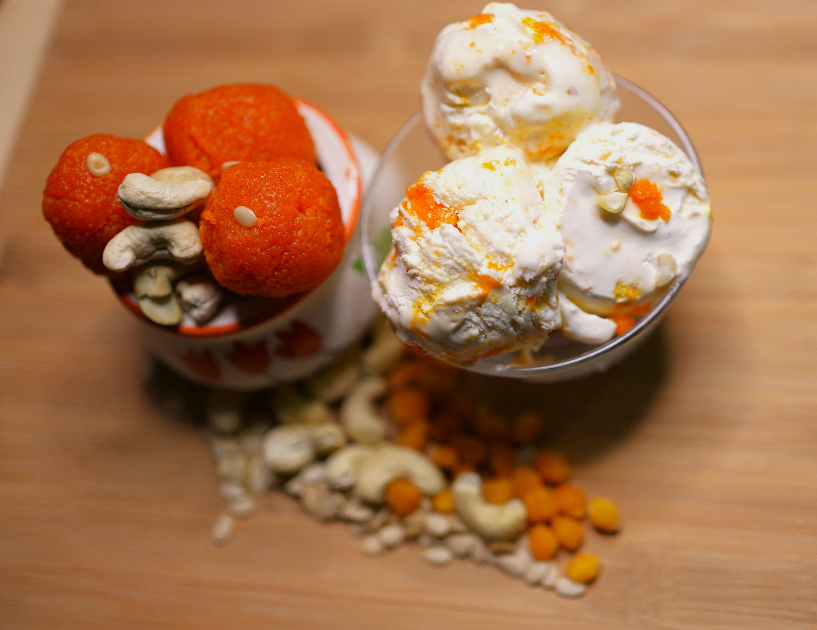 Top view of Indian laddoos and ice cream with cashews on a wooden surface.