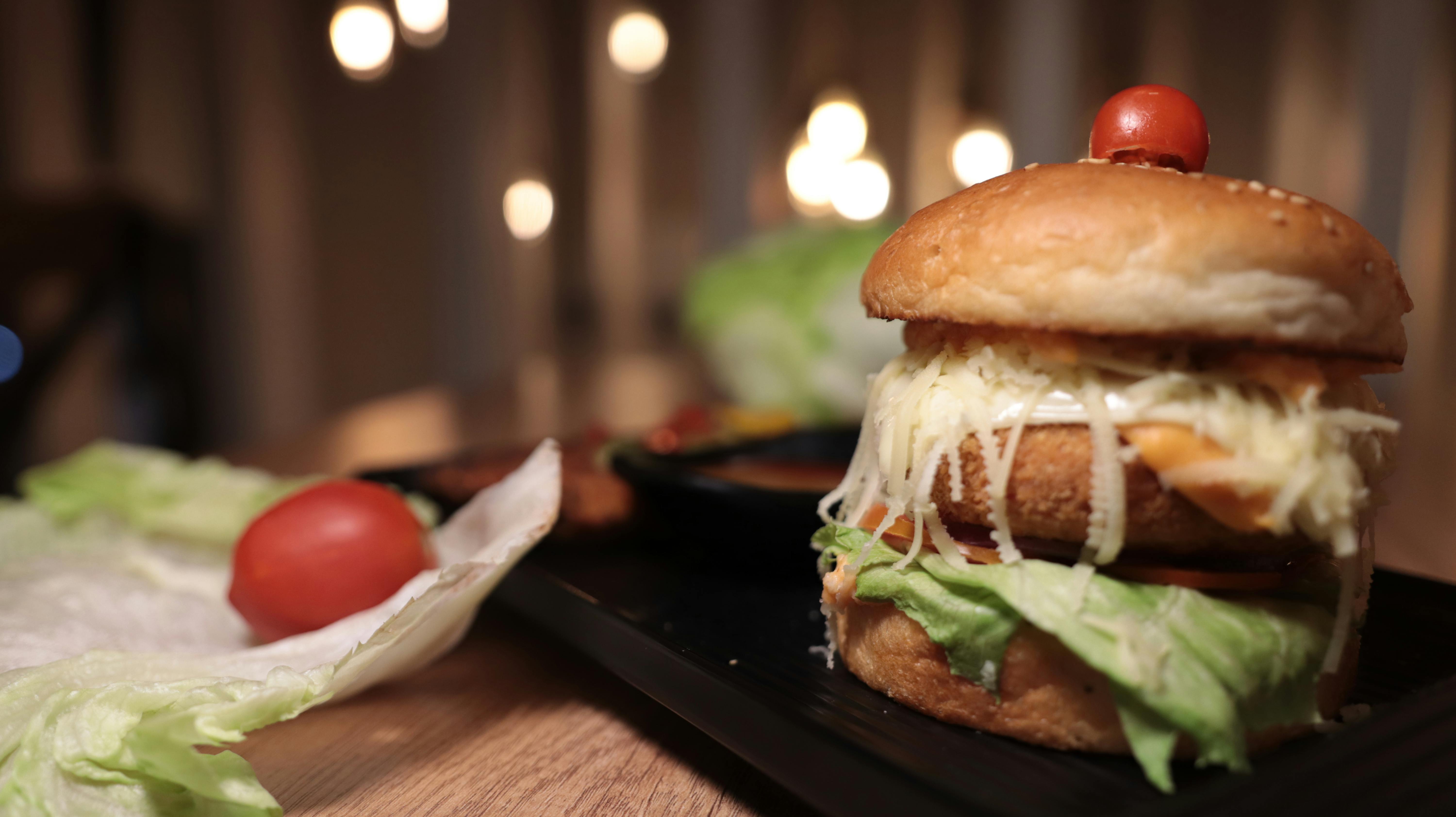 Gratuit Gros plan sur un hamburger gastronomique avec laitue, fromage et tomate, posé sur une table en bois. Photos