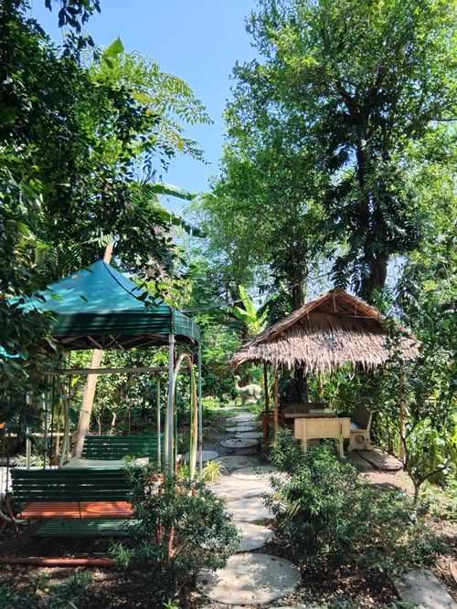 Free A peaceful garden scene featuring rustic huts surrounded by lush greenery under a clear blue sky. Stock Photo