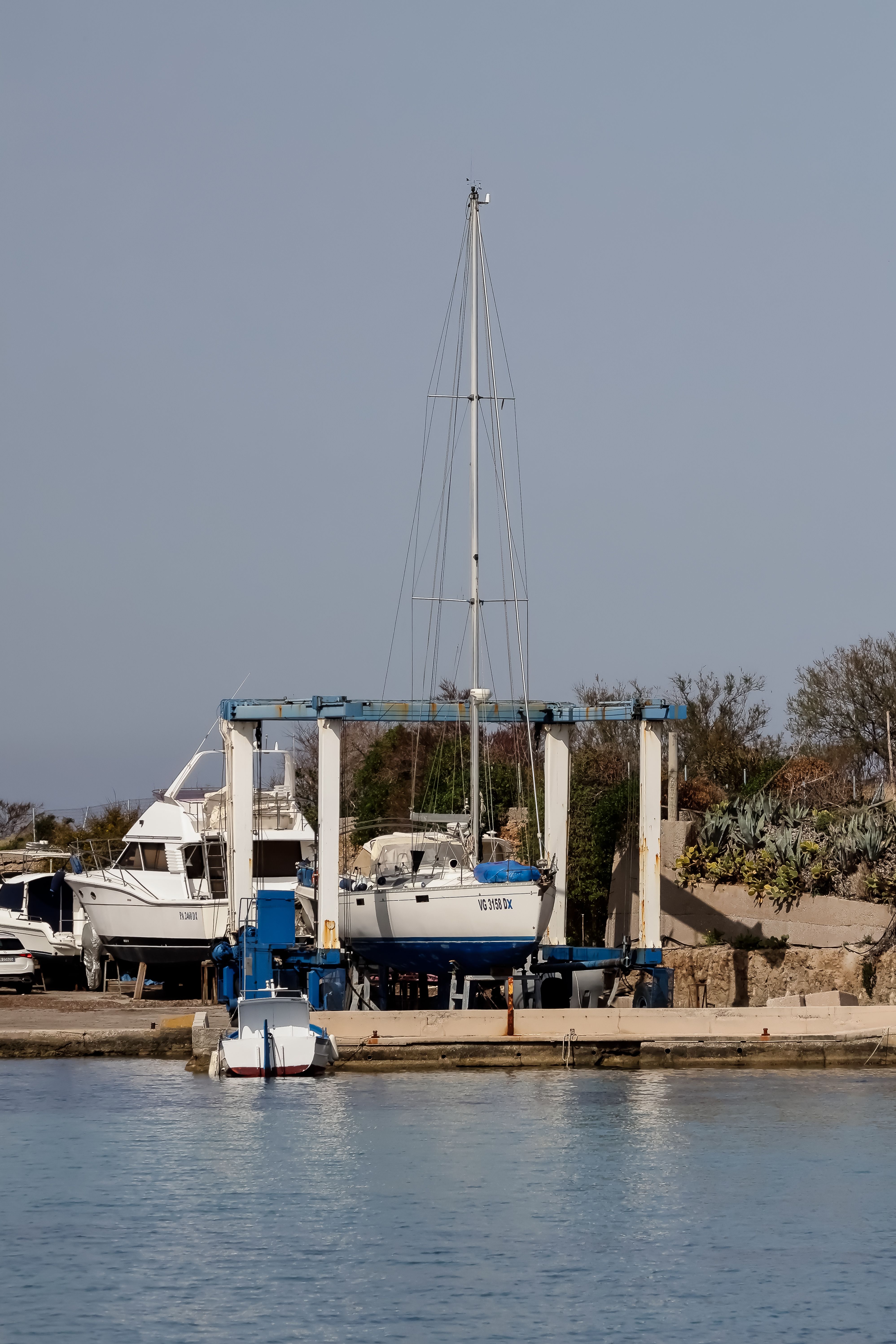 Sailboat hoisted in a boatyard travelift for haul-out and bottom work on a sunny day