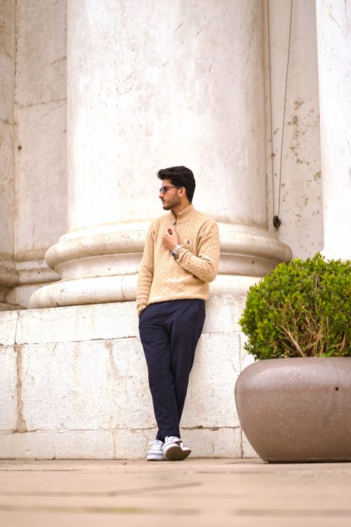 Free Fashionable man in sweater and jeans leans casually against a historical column in Italy. Stock Photo