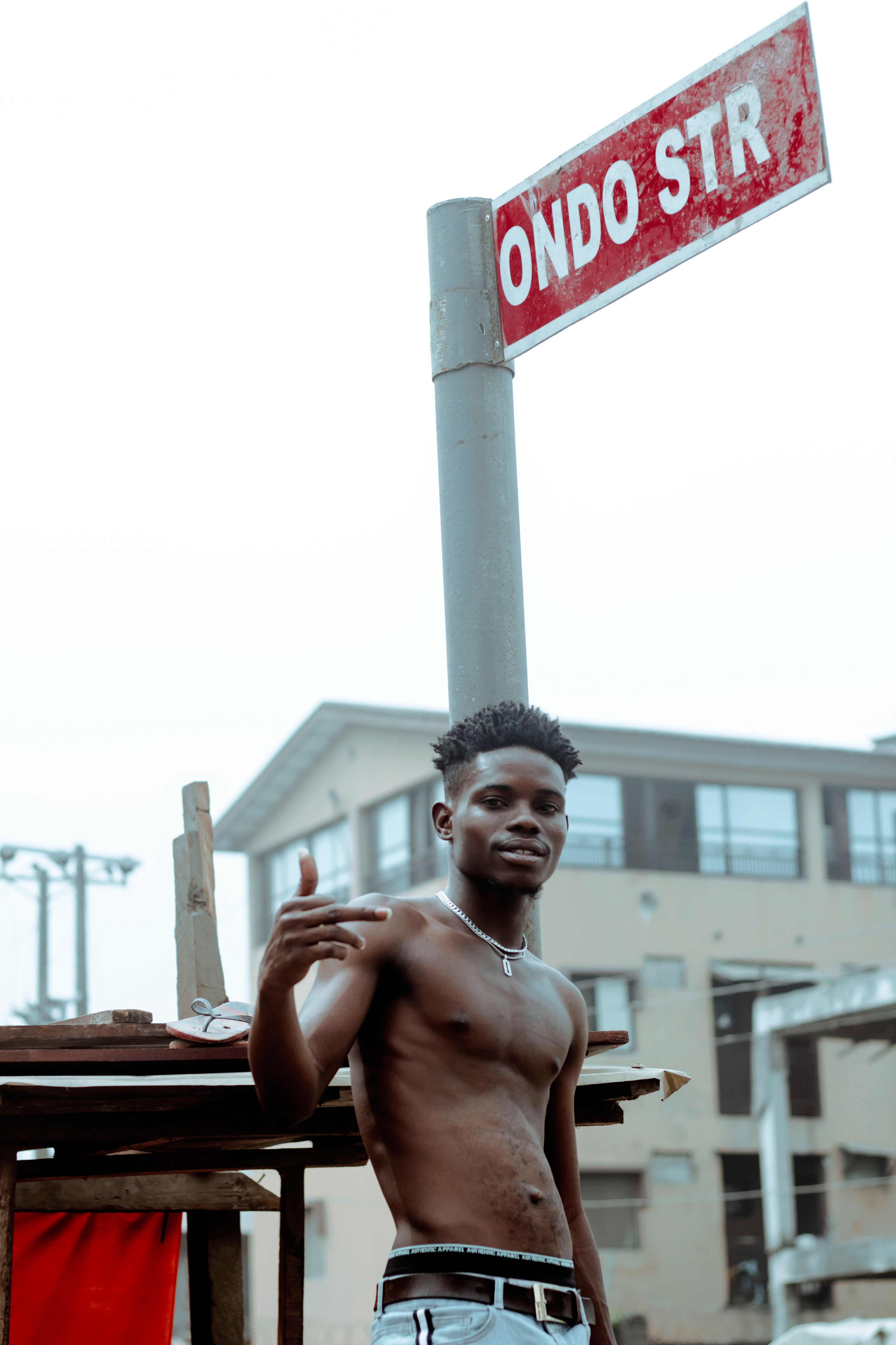 Shirtless man posing confidently on urban street under 'ONDO STR' sign.