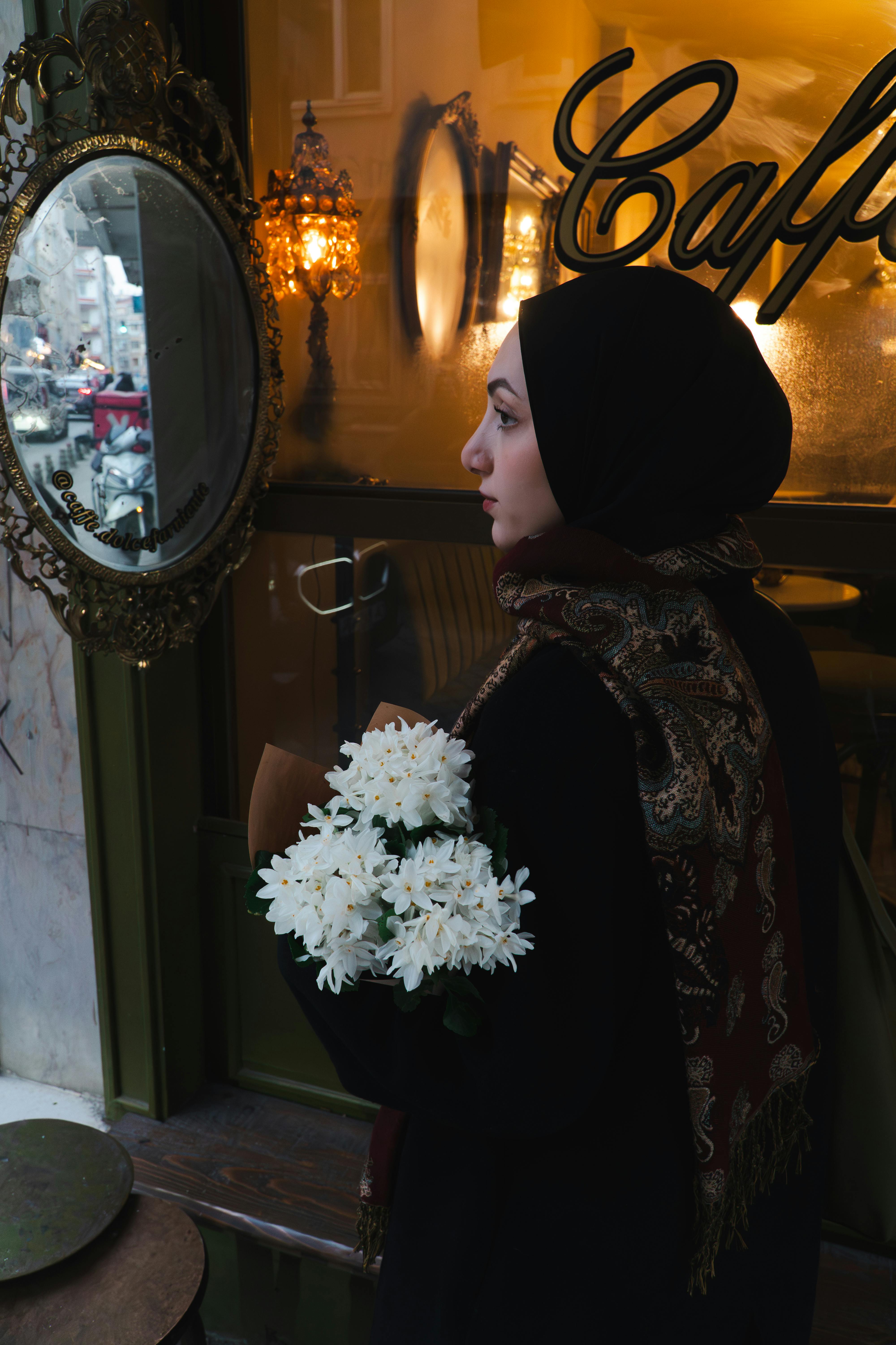 grátis Mulher de hijab segurando flores, refletindo do lado de fora de um aconchegante café em Istambul. Foto profissional
