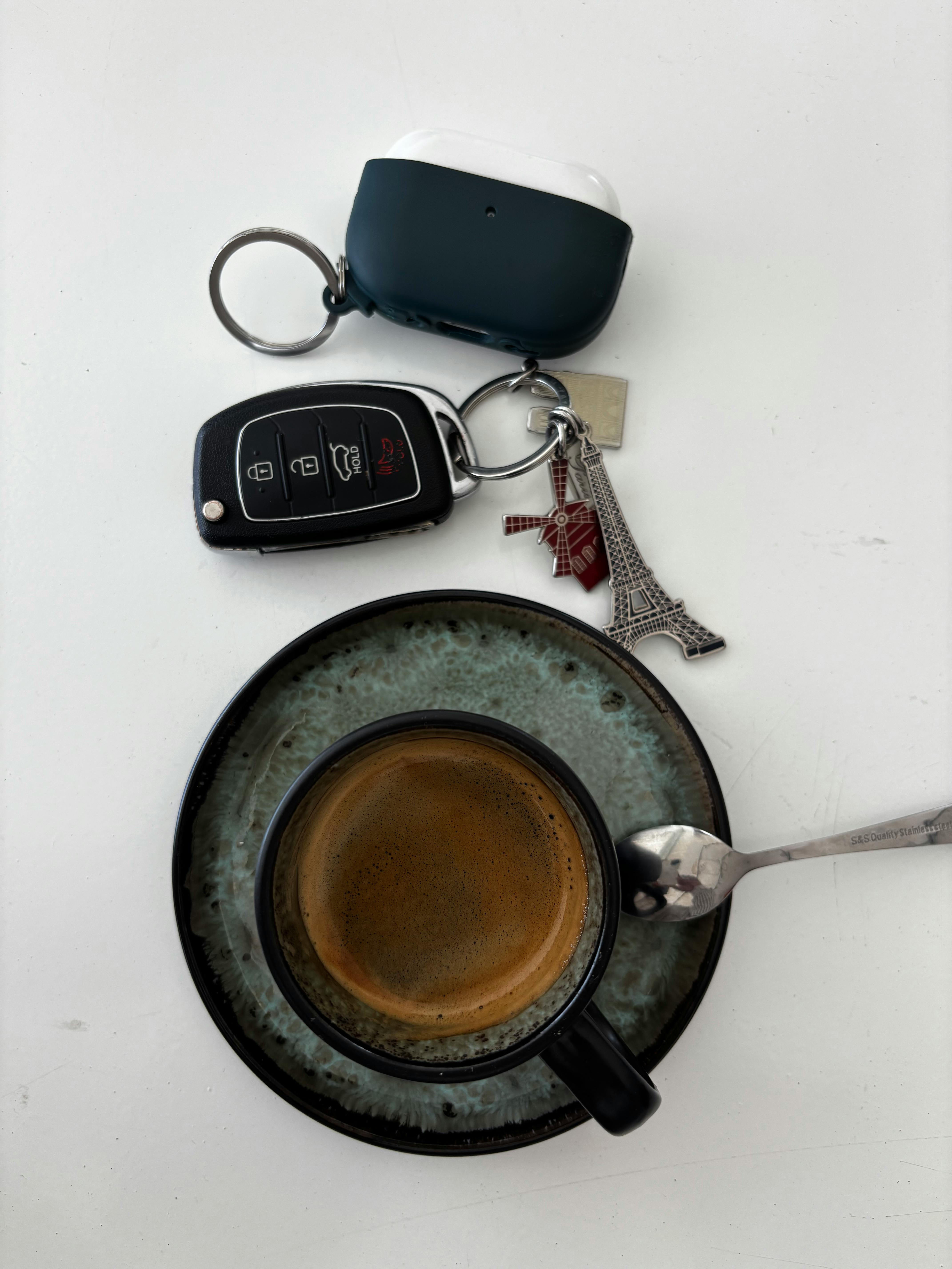 бесплатная Вид сверху на чашку эспрессо, автомобильные ключи и брелок с Эйфелевой башней на белой поверхности. Стоковое фото