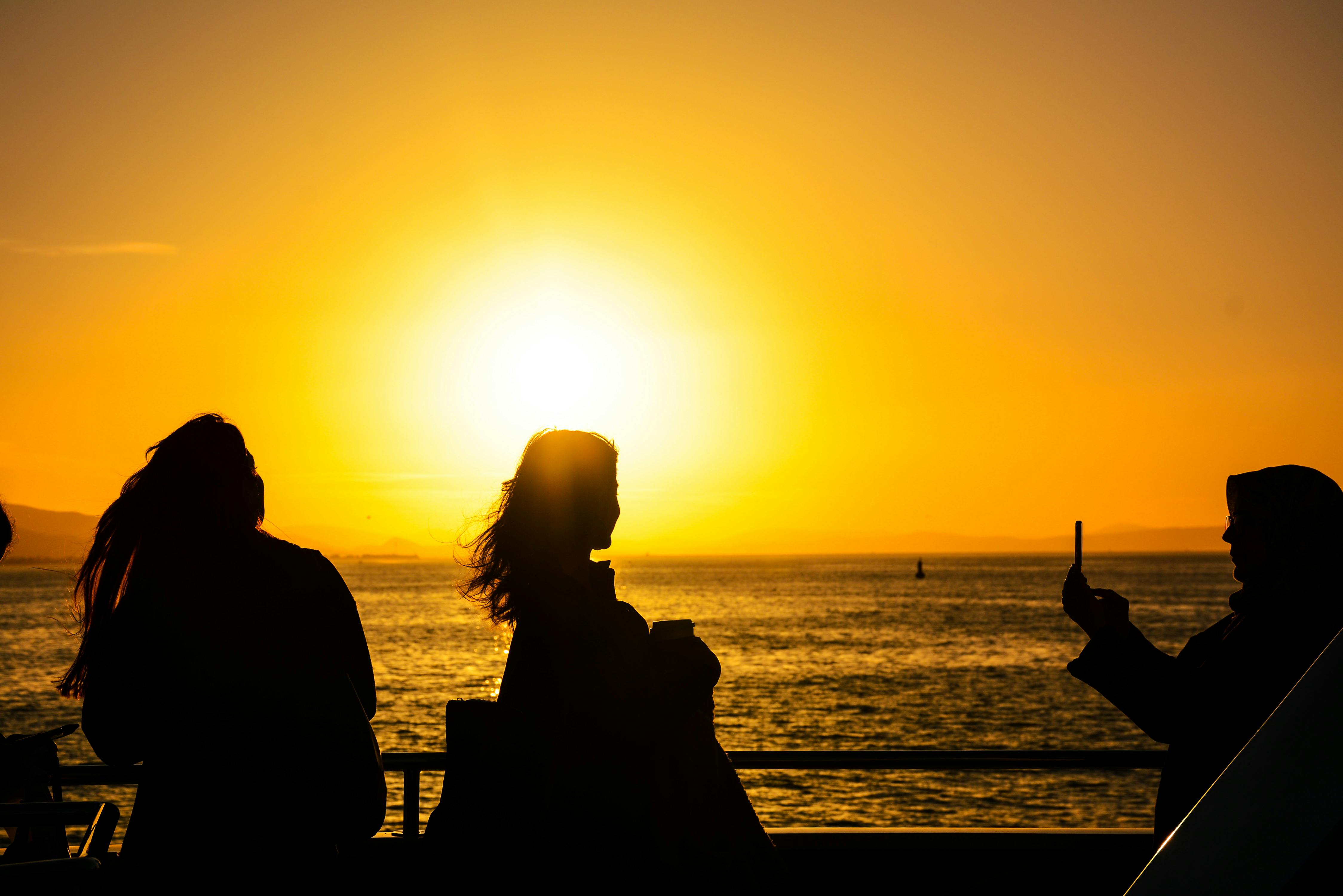 Gratis Cautivadoras siluetas de personas disfrutando de una puesta de sol junto al océano, perfectas para temas de viajes y estilo de vida. Foto de stock