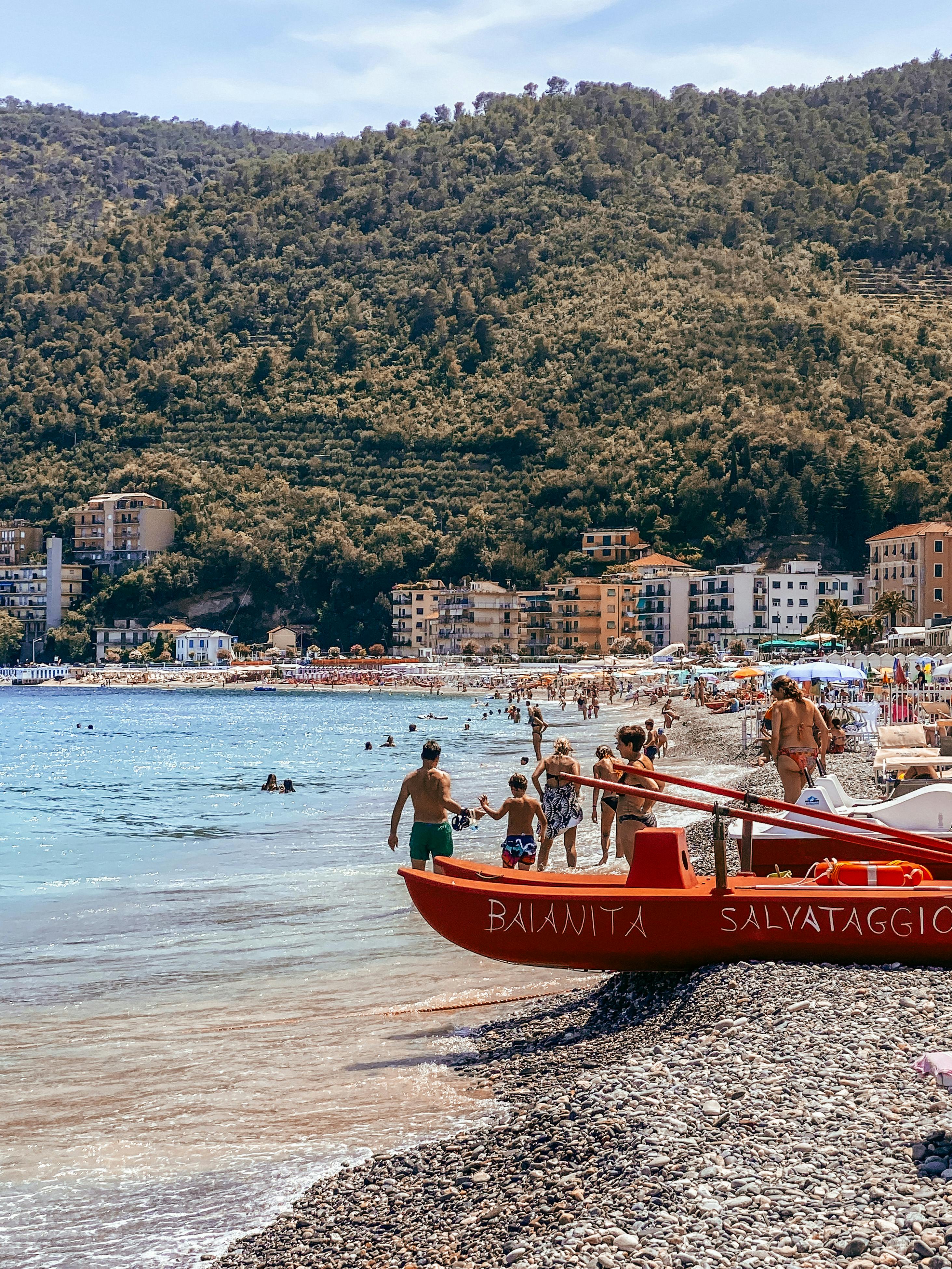 無料 地中海沿岸を楽しむ人々や赤いライフガードボートが写る、太陽が降り注ぐイタリアのビーチの風景。 写真素材