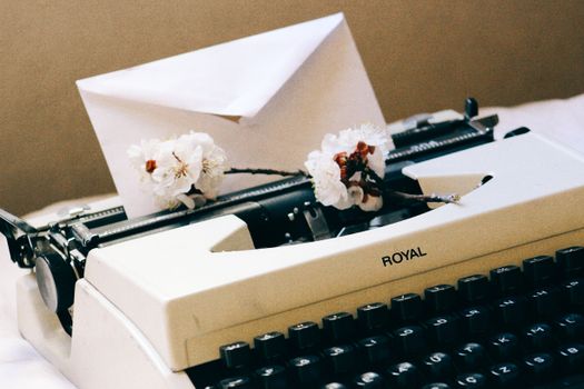 A classic typewriter adorned with cherry blossoms and an envelope, exuding a nostalgic feelings.