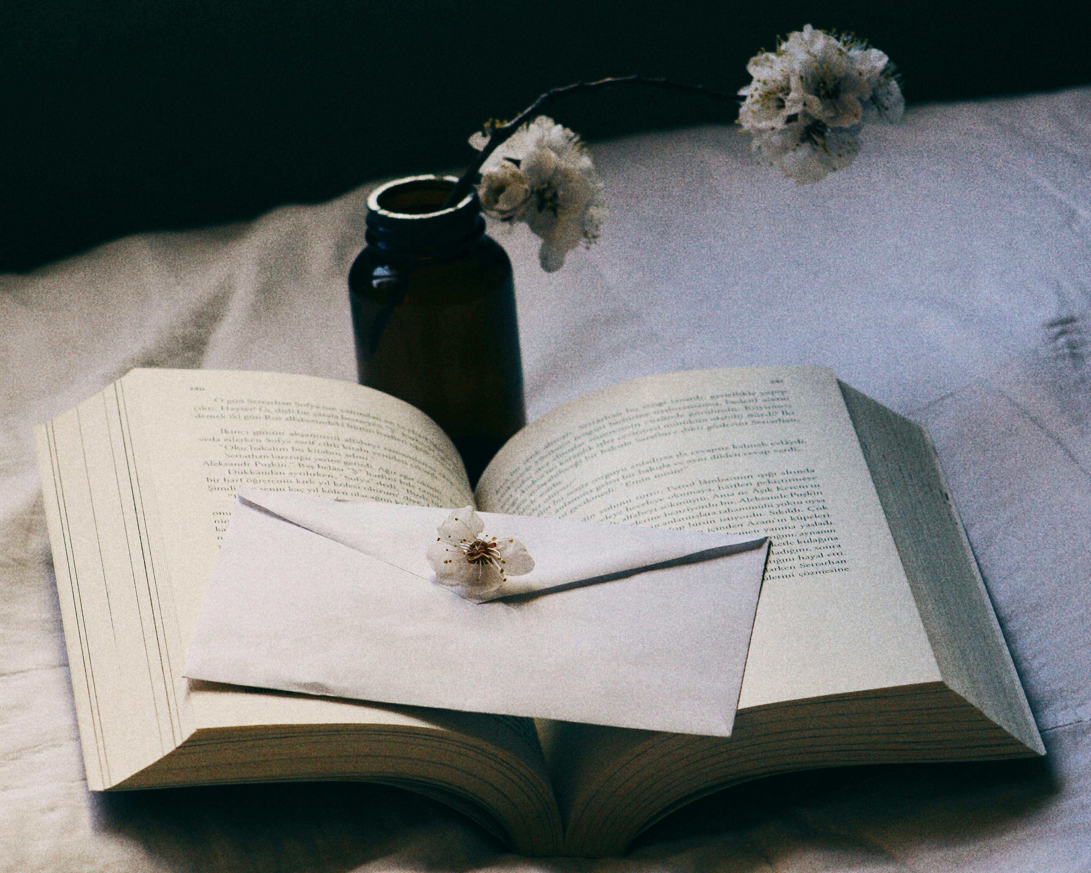 Gratis Una escena acogedora con un libro abierto, un sobre y flores sobre una cama, que evoca relajación. Foto de stock