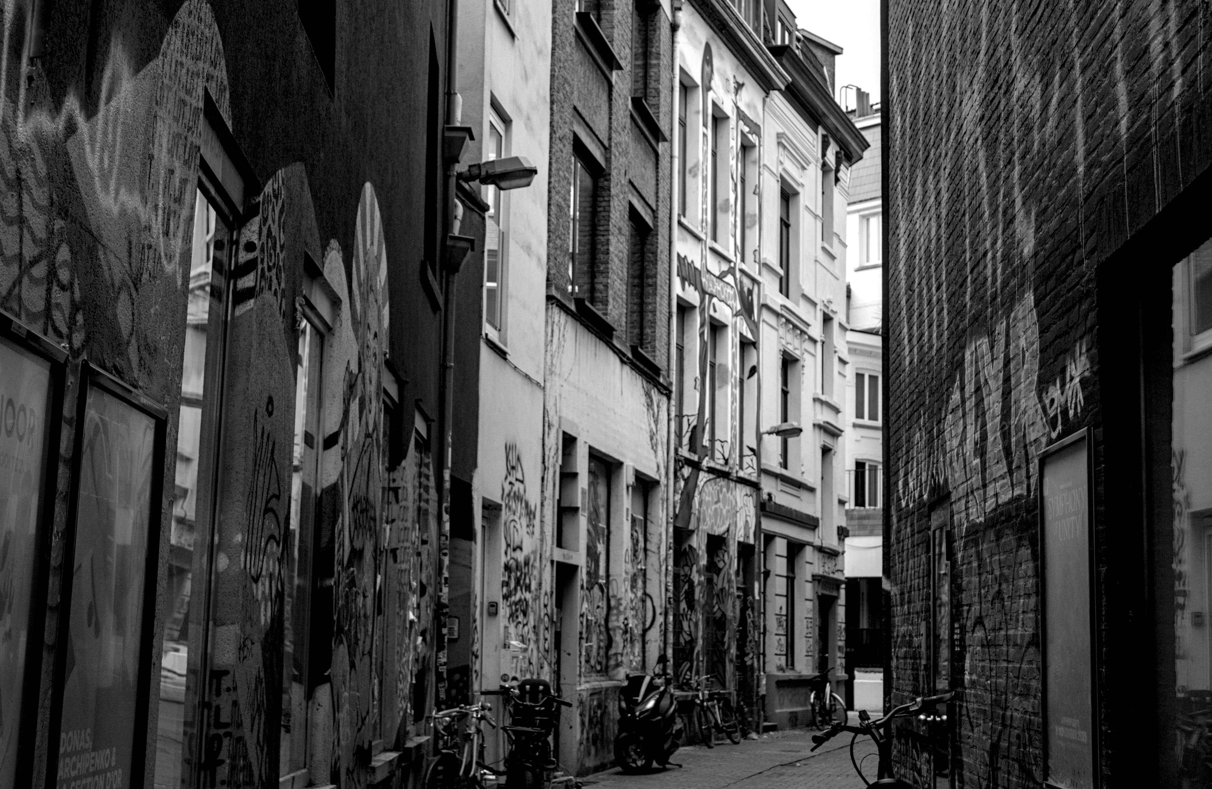 ingyenes Fekete-fehér fotó egy keskeny városi sikátorról, graffitivel borított falakkal és parkoló biciklikkel. Stockfotó