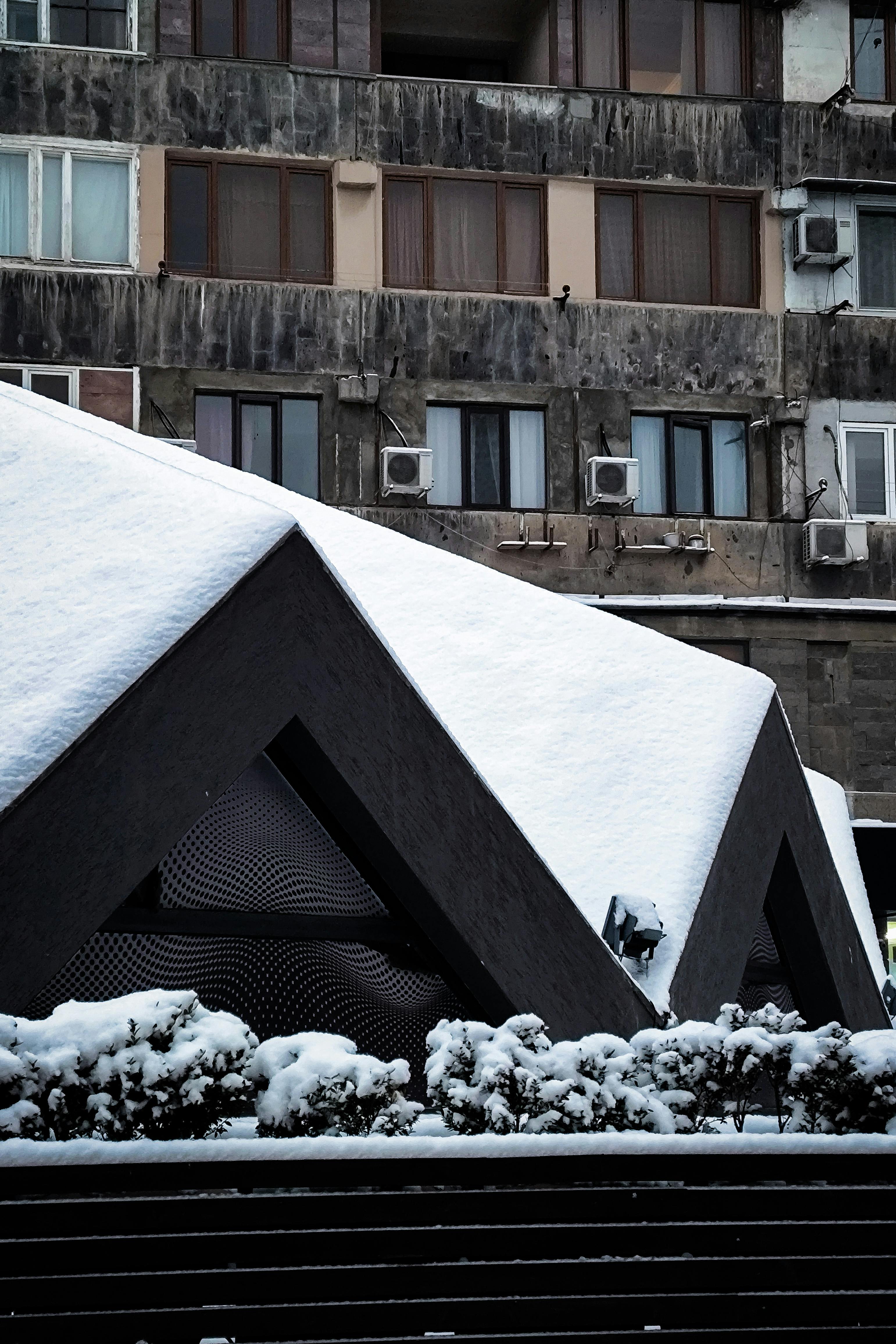 gratis Geometrisch gebouw bedekt met sneeuw, met op de achtergrond stedelijke woonblokken. Stockfoto