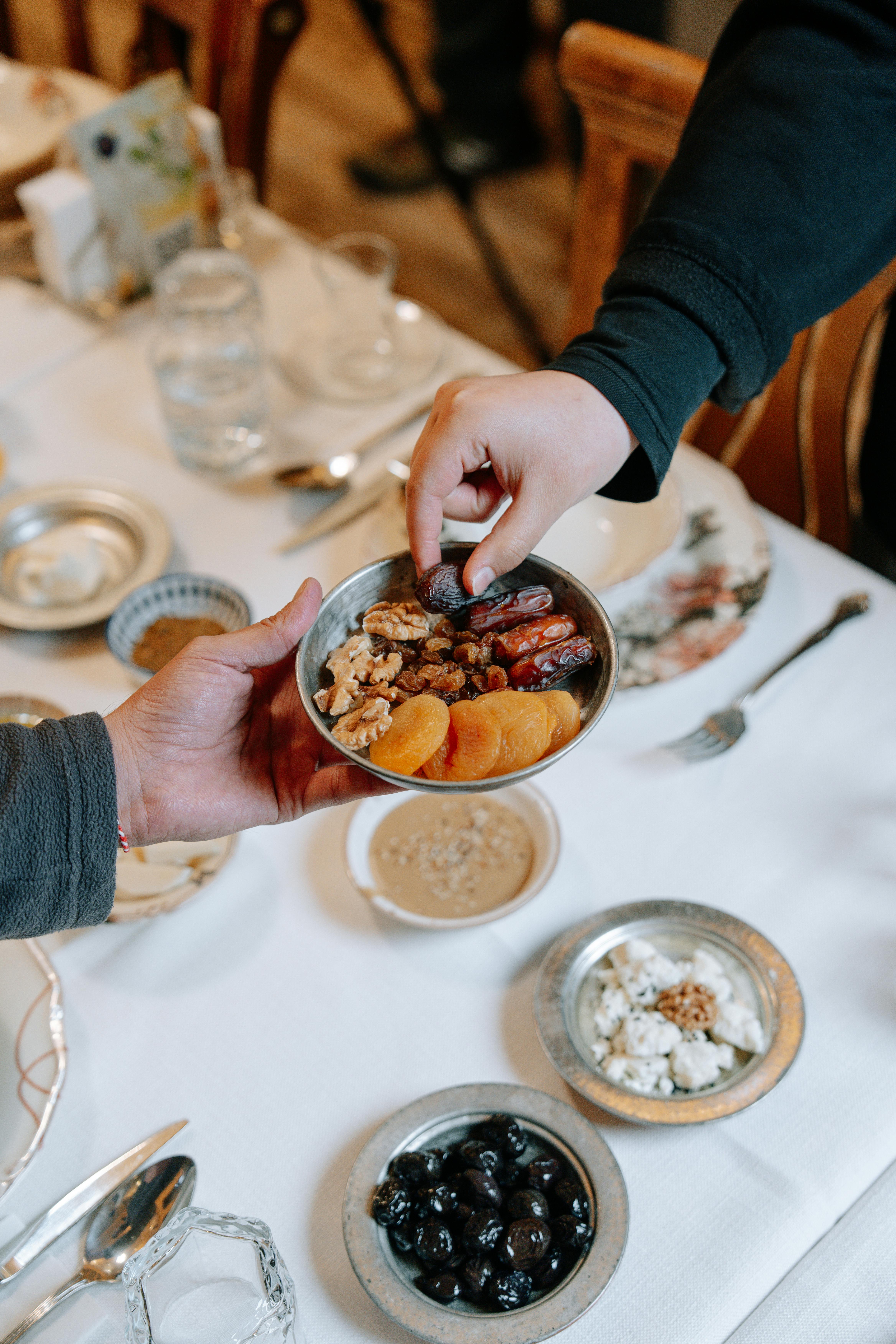 De franc Mans compartint un bol de fruites seques i fruits secs sobre una taula parada, simbolitzant la generositat. Foto d'estoc