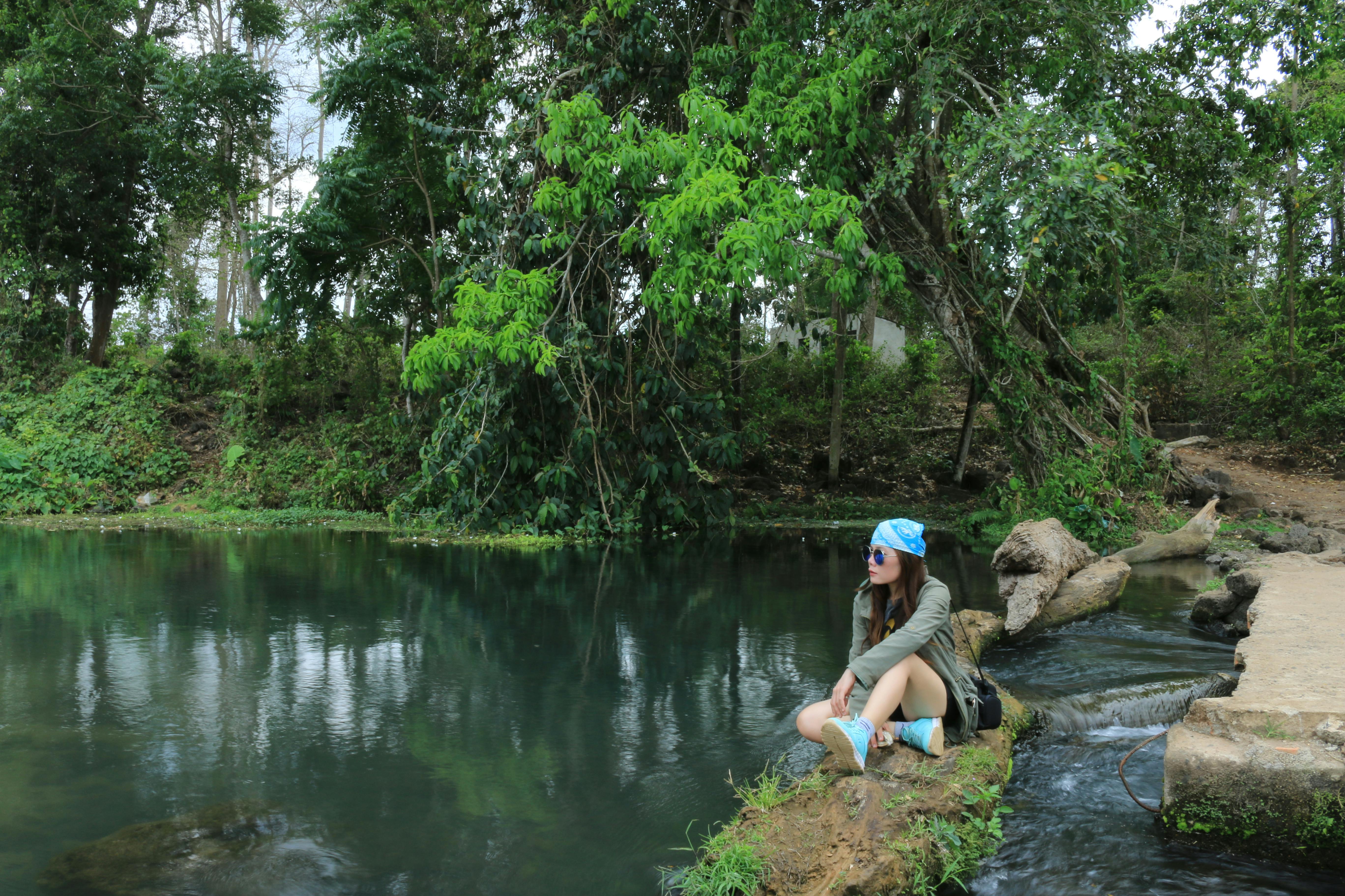 Bezpłatne Młoda kobieta odpoczywa nad spokojnym strumieniem w Wietnamie, otoczona bujną zielenią. Zdjęcie z galerii