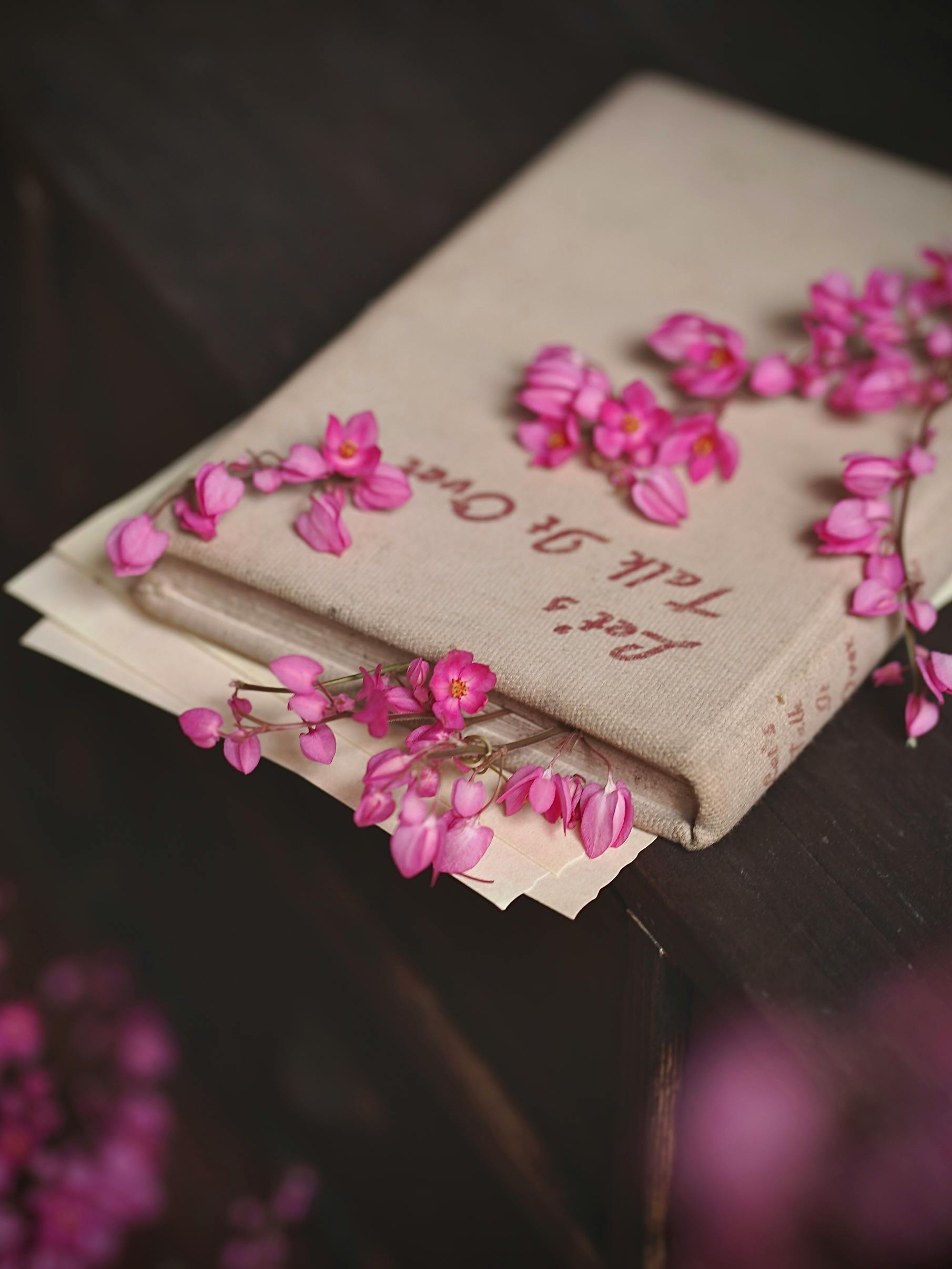 gratis Een vintage boek, versierd met levendige roze bloemen op een rustieke houten ondergrond, creëert een nostalgische en romantische sfeer. Stockfoto