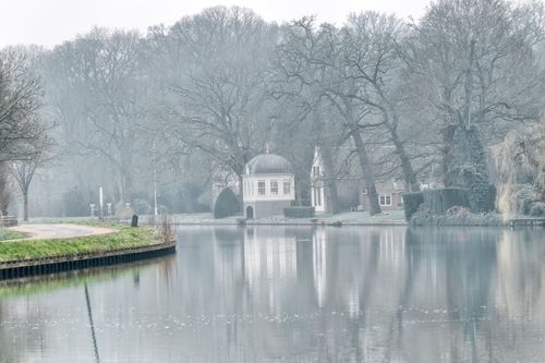 Free Serene winter landscape by a lake with bare trees and classical building reflection. Stock Photo