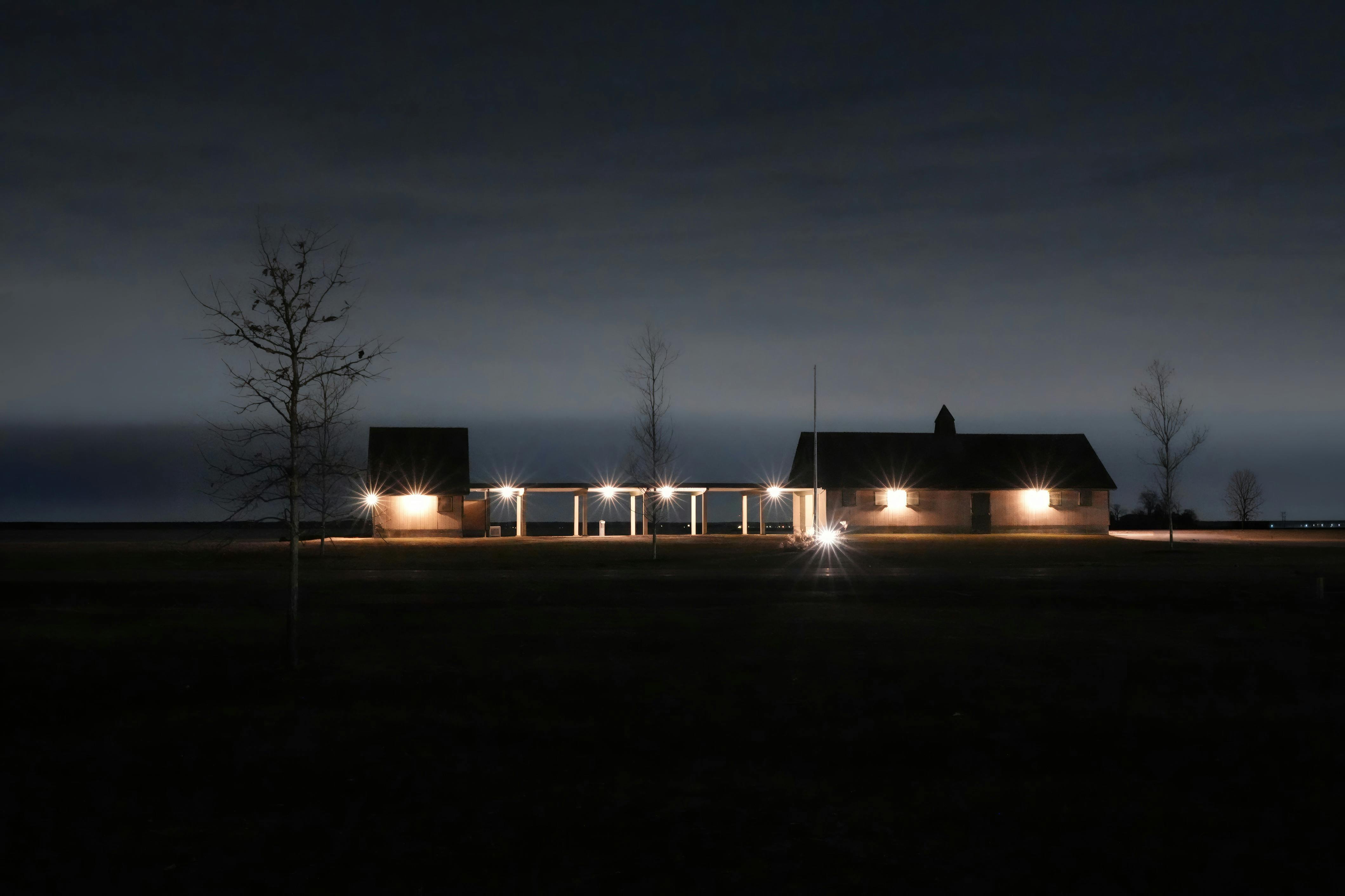 Miễn phí Một khung cảnh đêm thanh bình với một tòa nhà được thắp sáng giữa cánh đồng rộng mở dưới bầu trời trong xanh. Ảnh lưu trữ