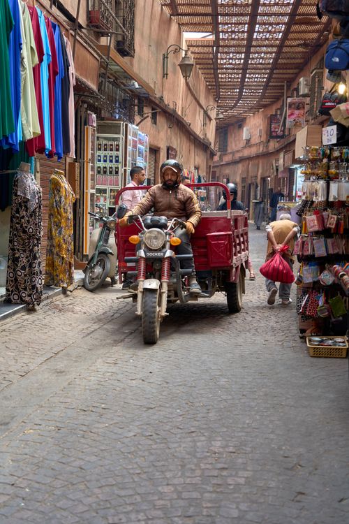 Free Vibrant market street in Marrakesh bustling with people, vehicles, and colorful stalls. Stock Photo