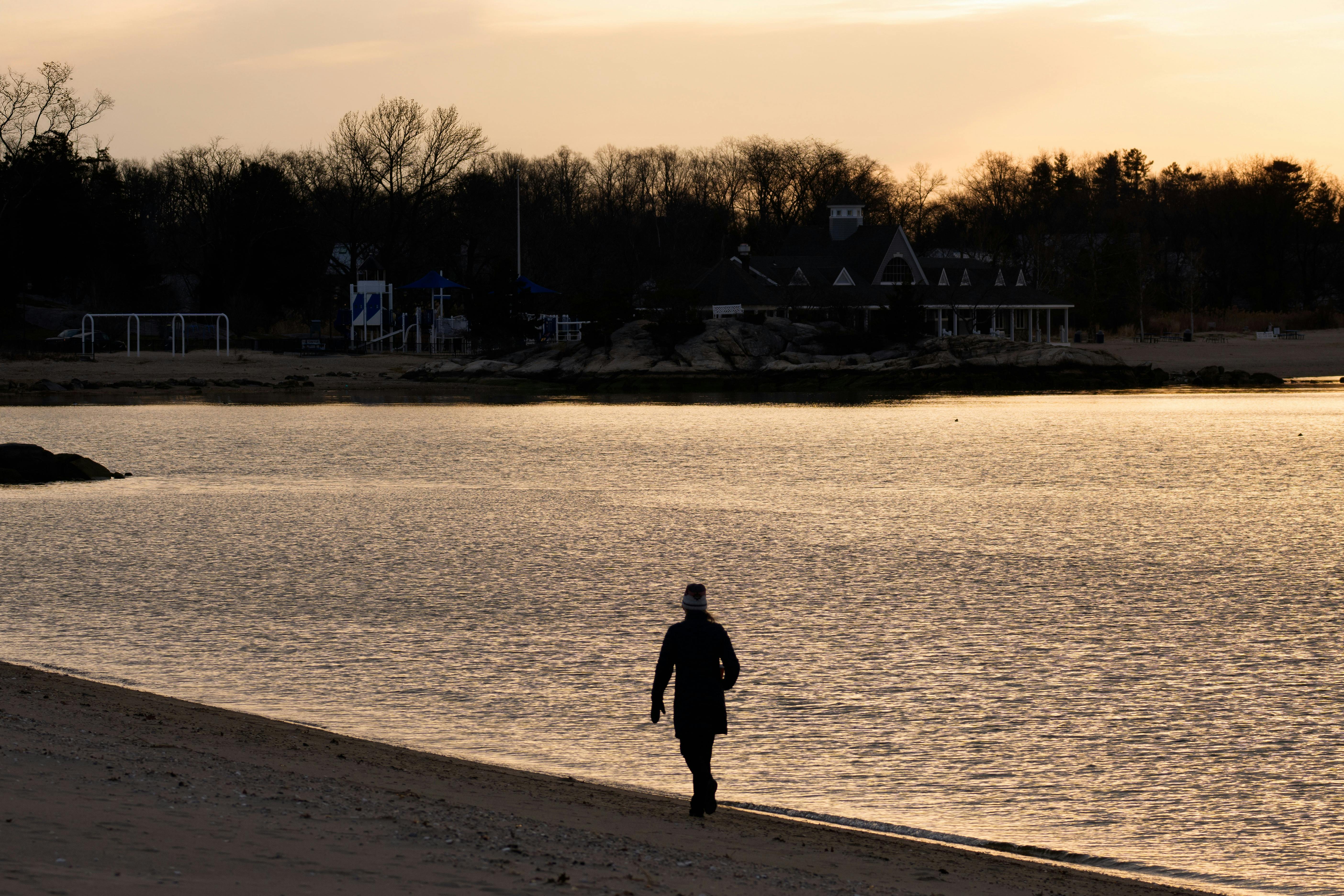 Gratis Silhuet af en person, der går langs stranden ved solopgang i Stamford's Cove Island Park. Lagerfoto