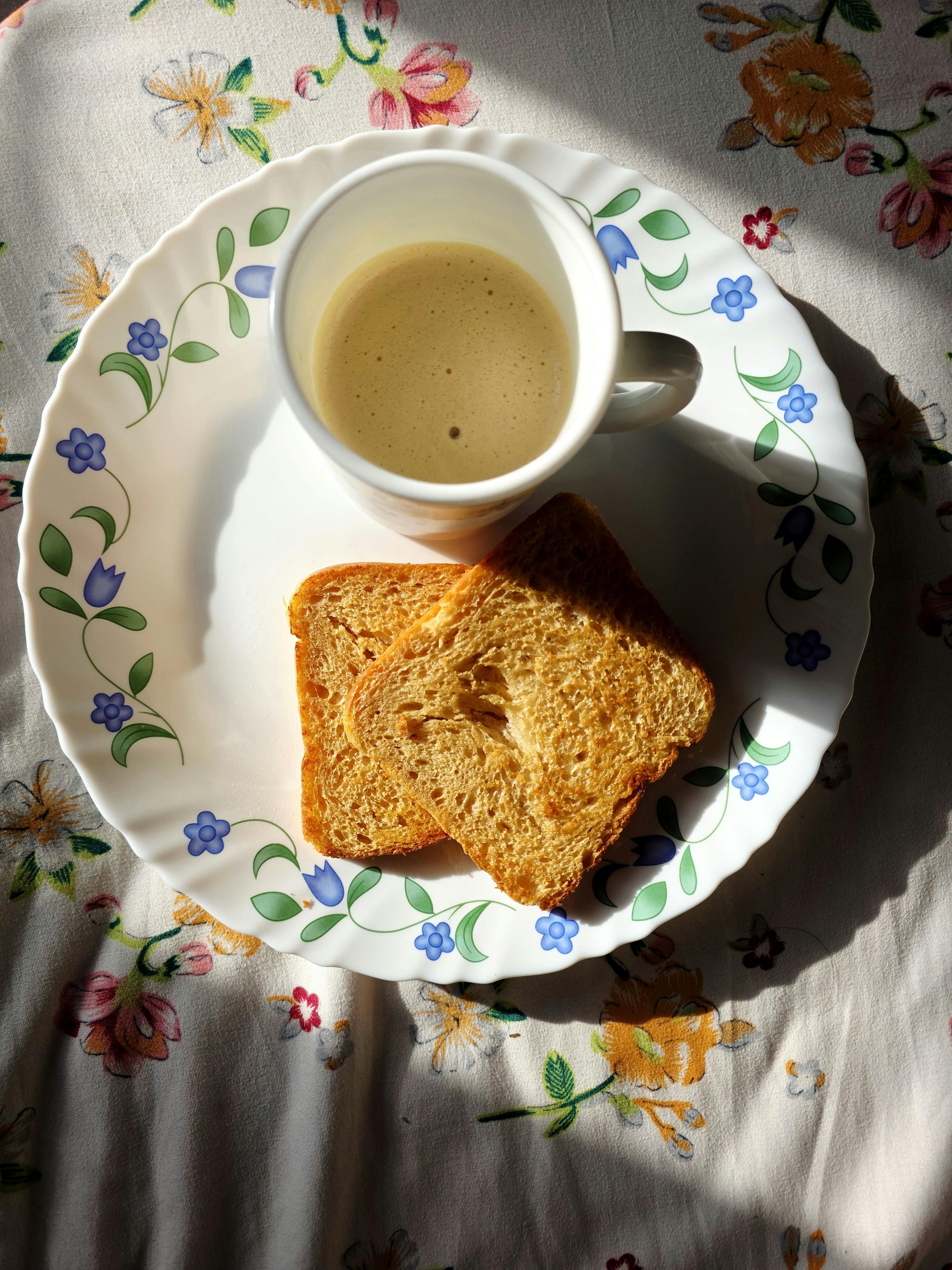 Kostnadsfria En mysig frukostdukning med kaffe och rostat bröd på en blommig duk. Stock foto