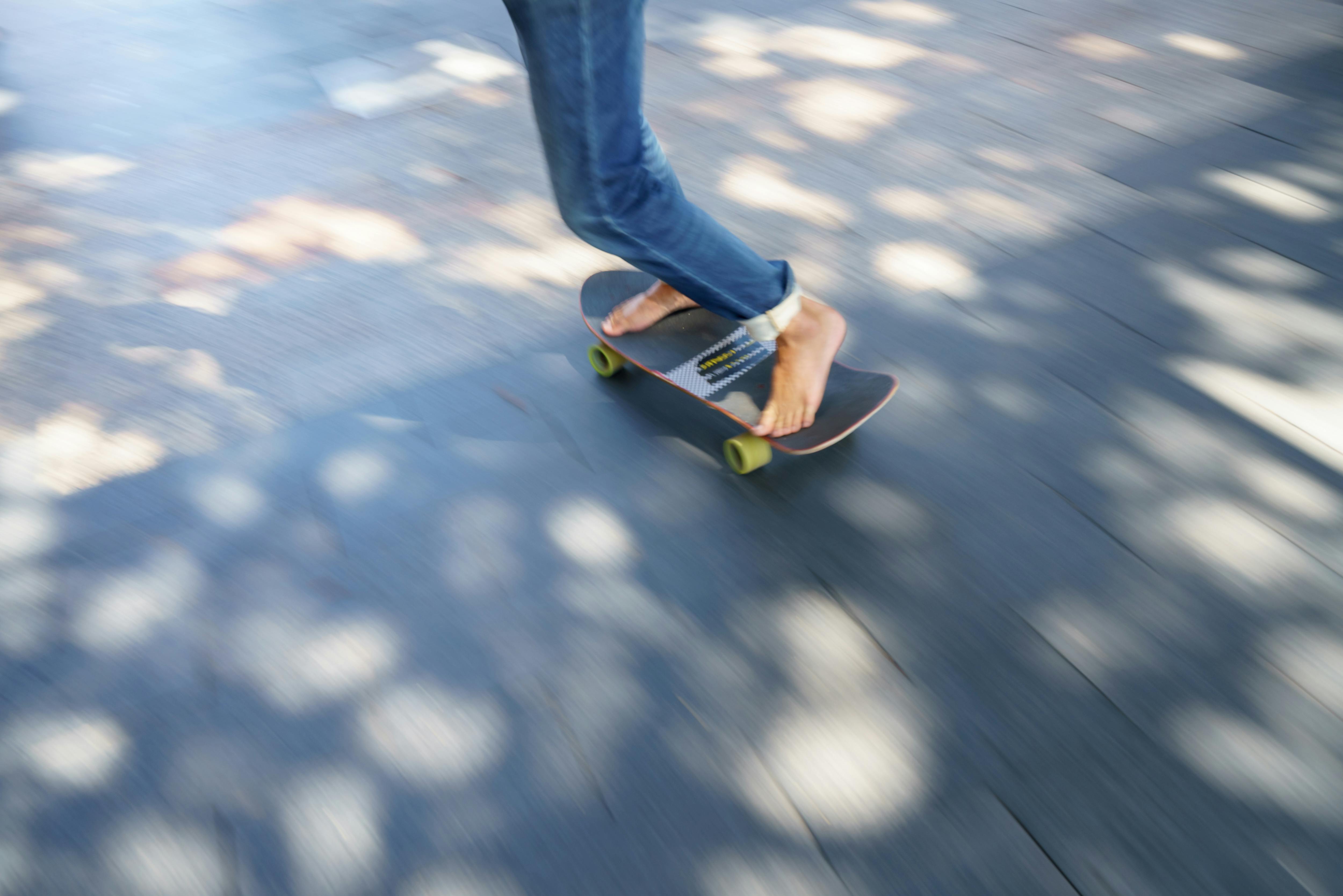 bezplatná Dynamický záběr osoby jedoucí na skateboardu naboso na sluncem zalité městské ulici. Základová fotografie