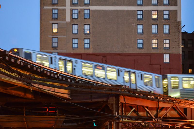 Blurred motion of an elevated train speeding through the city in the evening, with buildings in the background.