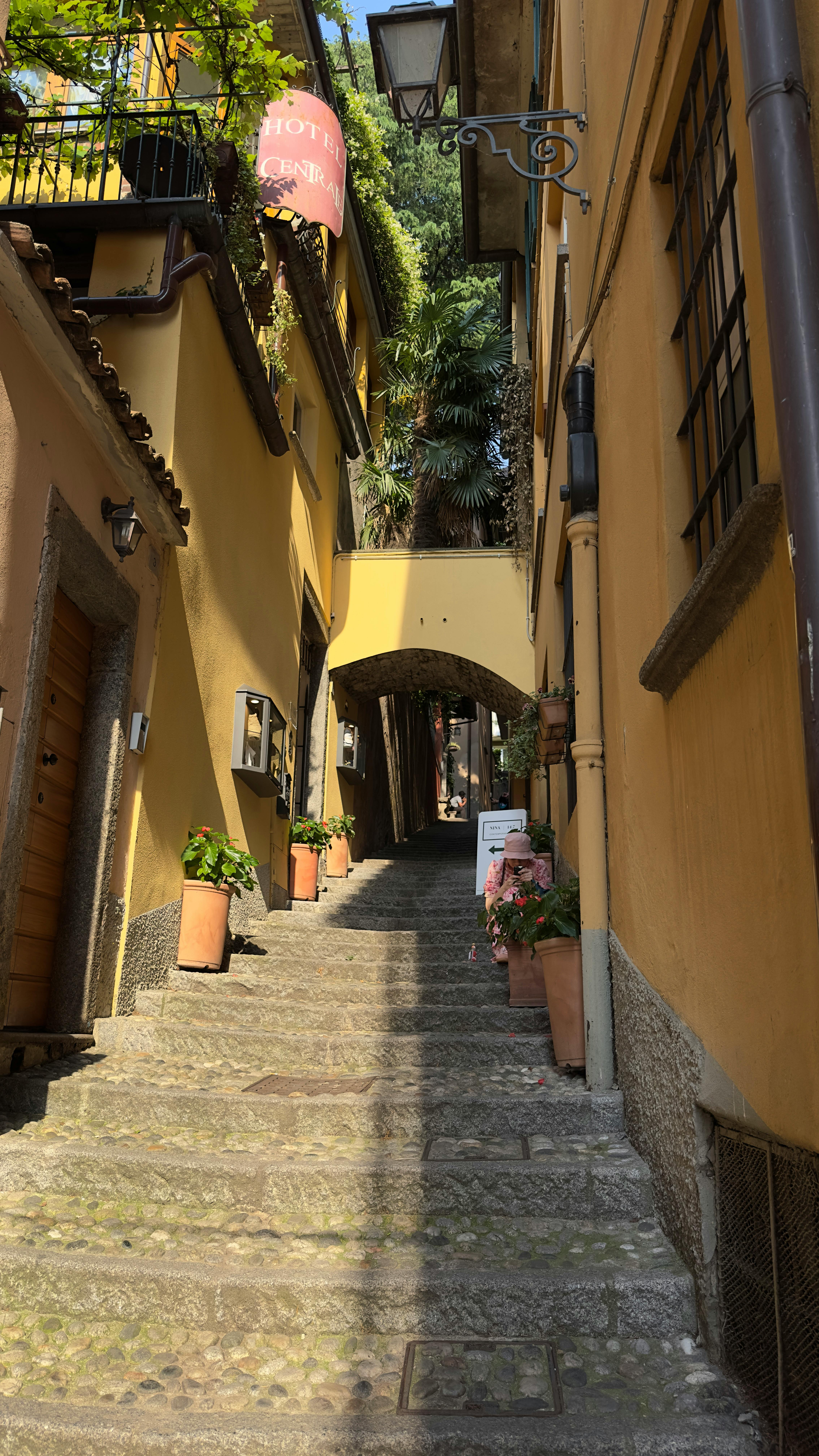 Gratis Brosteinsgate i Bellagio, Italia, med historisk arkitektur og fargerike blomsterpotter. Arkivbilde